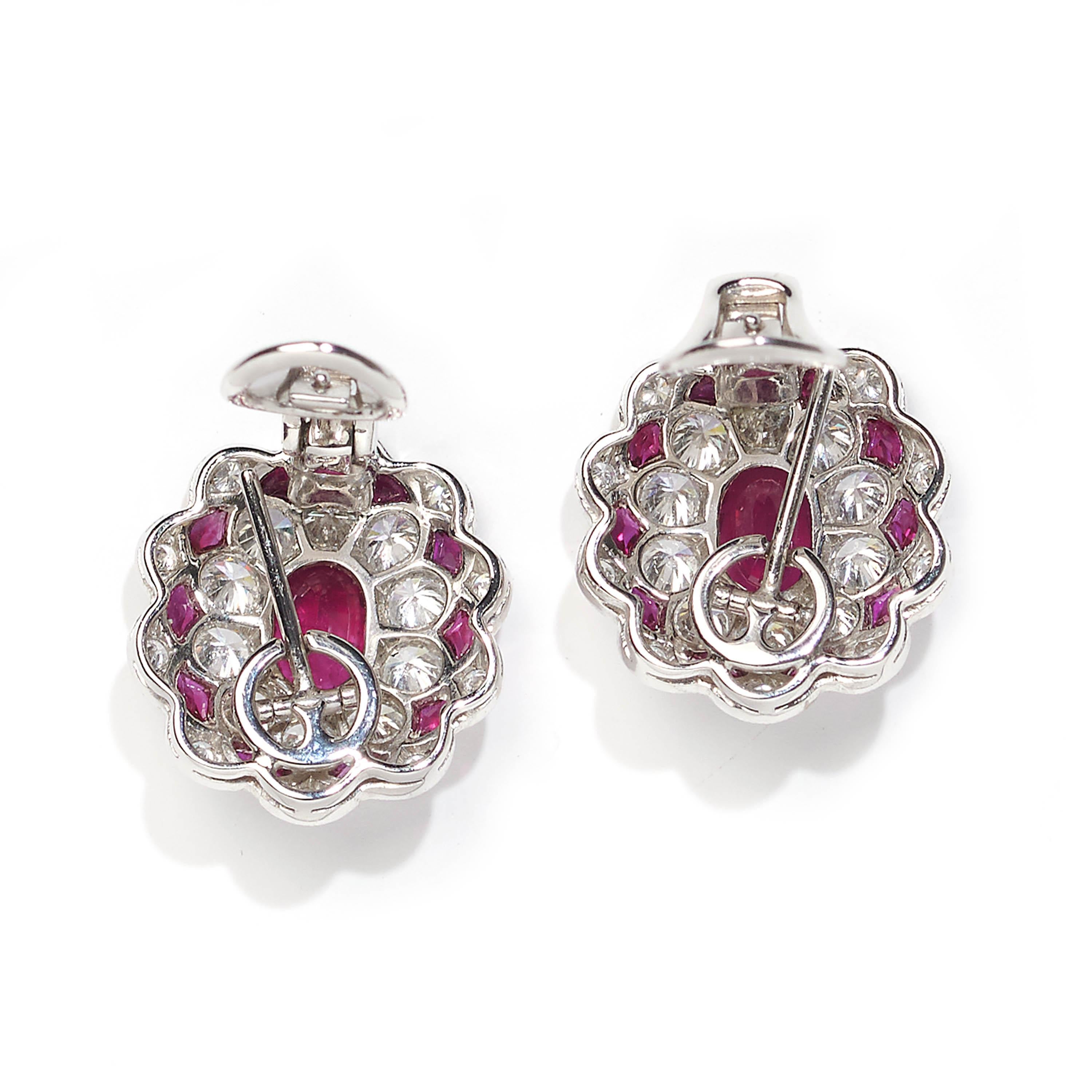 A pair of modern cluster earrings, set with oval rubies weighing a total of 2.51 carats, surrounded by fancy-cut rubies weighing a total of 0.81 carats, and round diamonds weighing a total of 2.71 carats, with posts and hinged clip fittings, mounted