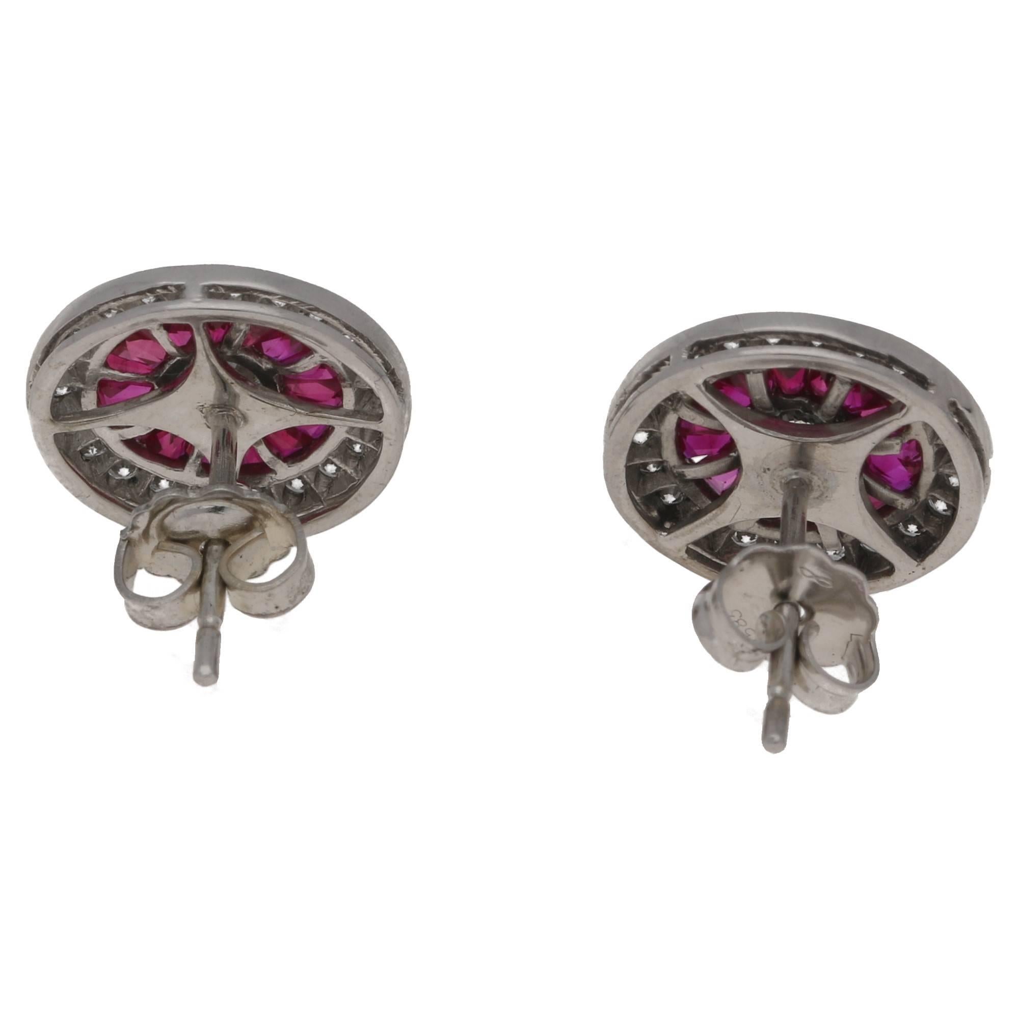 A beautiful pair of ruby and diamond target cluster earrings. The earrings are formed of a round brilliant cut diamond centrally set in a spectacle setting. The central diamond is surrounded buy a row of calibre cut rubies and further embellished