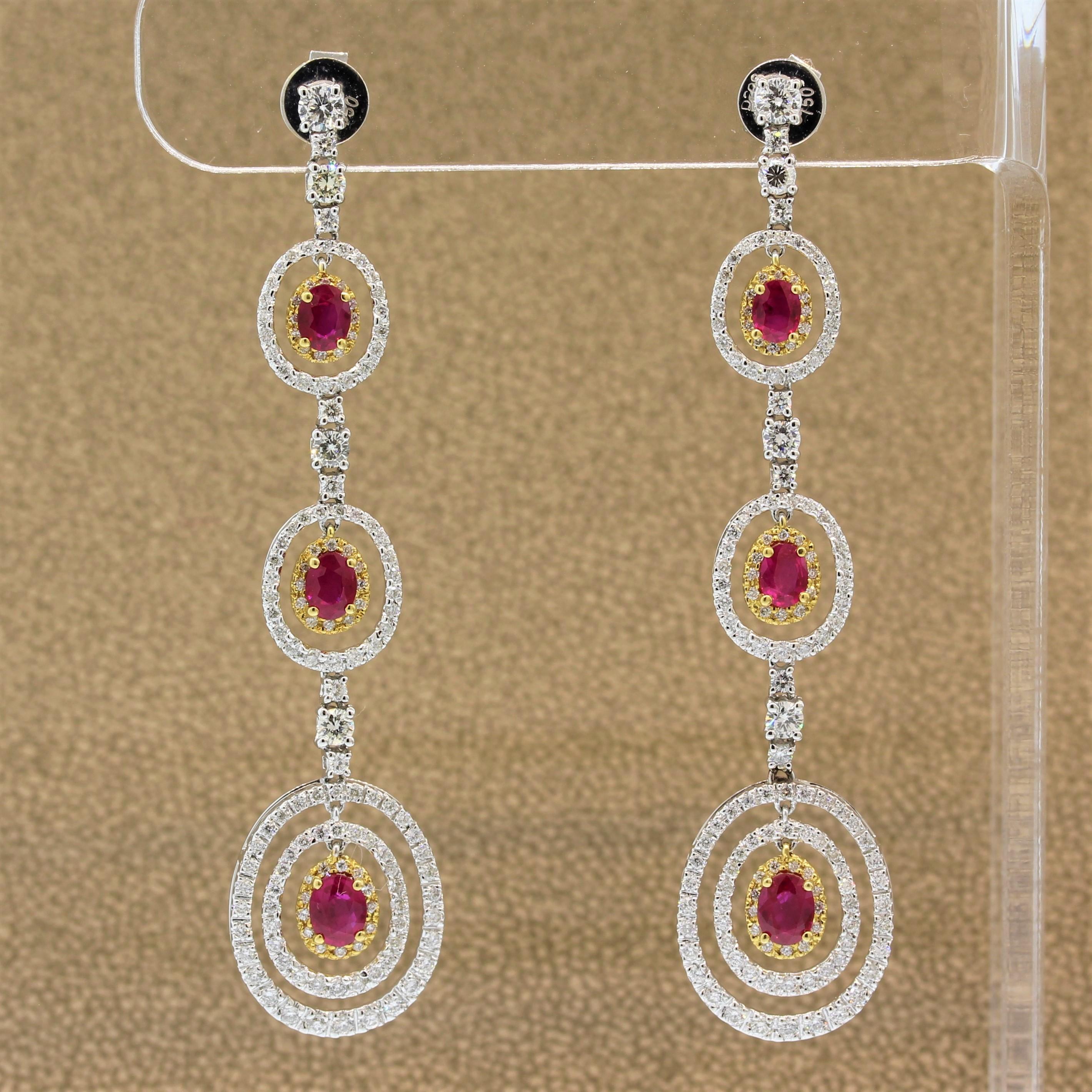 An elegant pair of drop earrings featuring vivid red rubies and round brilliant cut diamonds. There are 1.99 carats of oval shaped rubies set in 18K yellow gold. They are haloed and accented by 2.08 carats of diamonds which are VS in clarity and