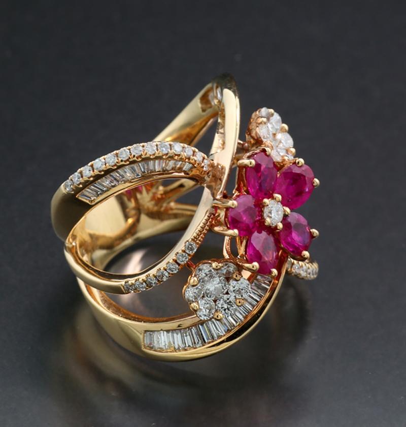 A stunning ring featuring 5 oval cut rubies, approx. 1.00 carat in total. The gemstones, displaying a vibrant transparent red-pinkish color, form a flower shape with a diamond at the center. On each side, there are two more diamond-decorated