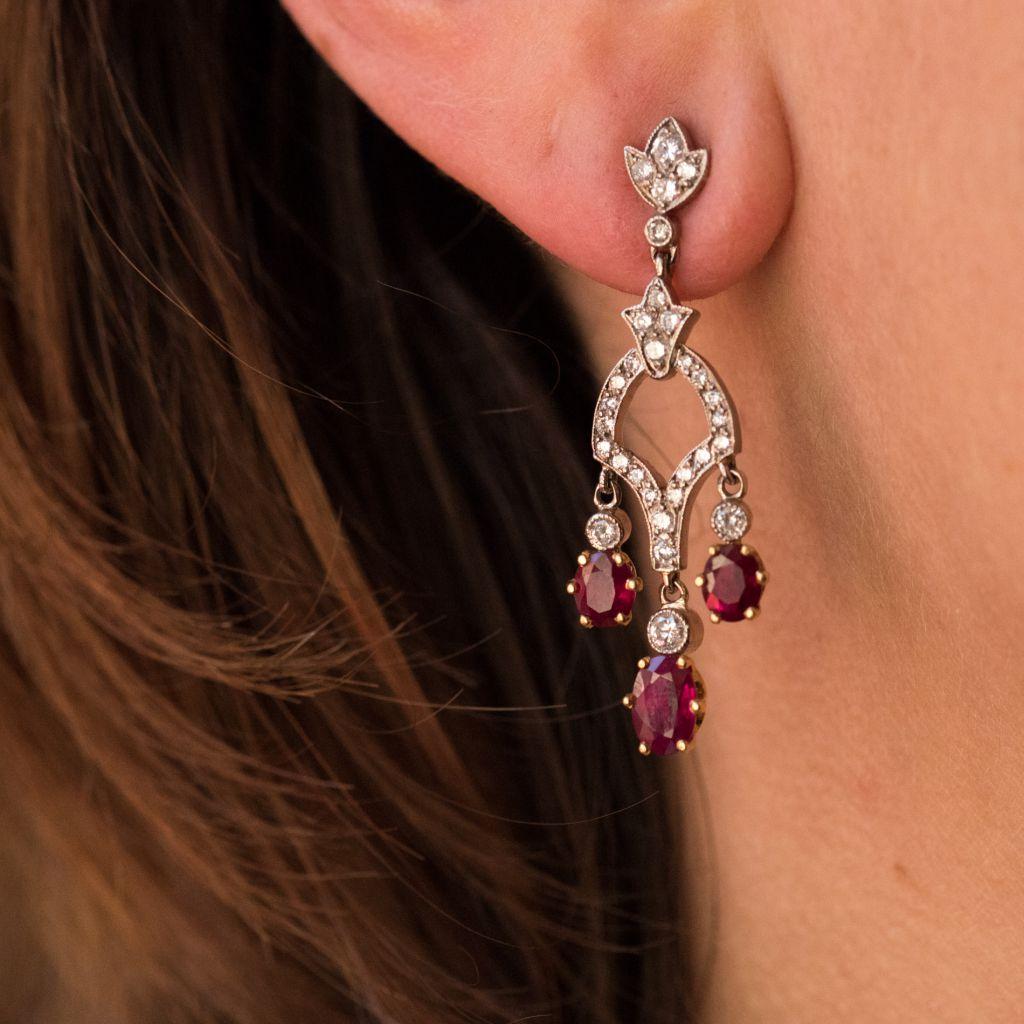 For pierced ears.
Earrings in 18 karat white gold, eagle head hallmark. 
Each earring features a small leaf set with diamonds at the base of which is a diamond decorated motif with 3 suspended claw set rubies. These earrings have alpa clasps. 
Total