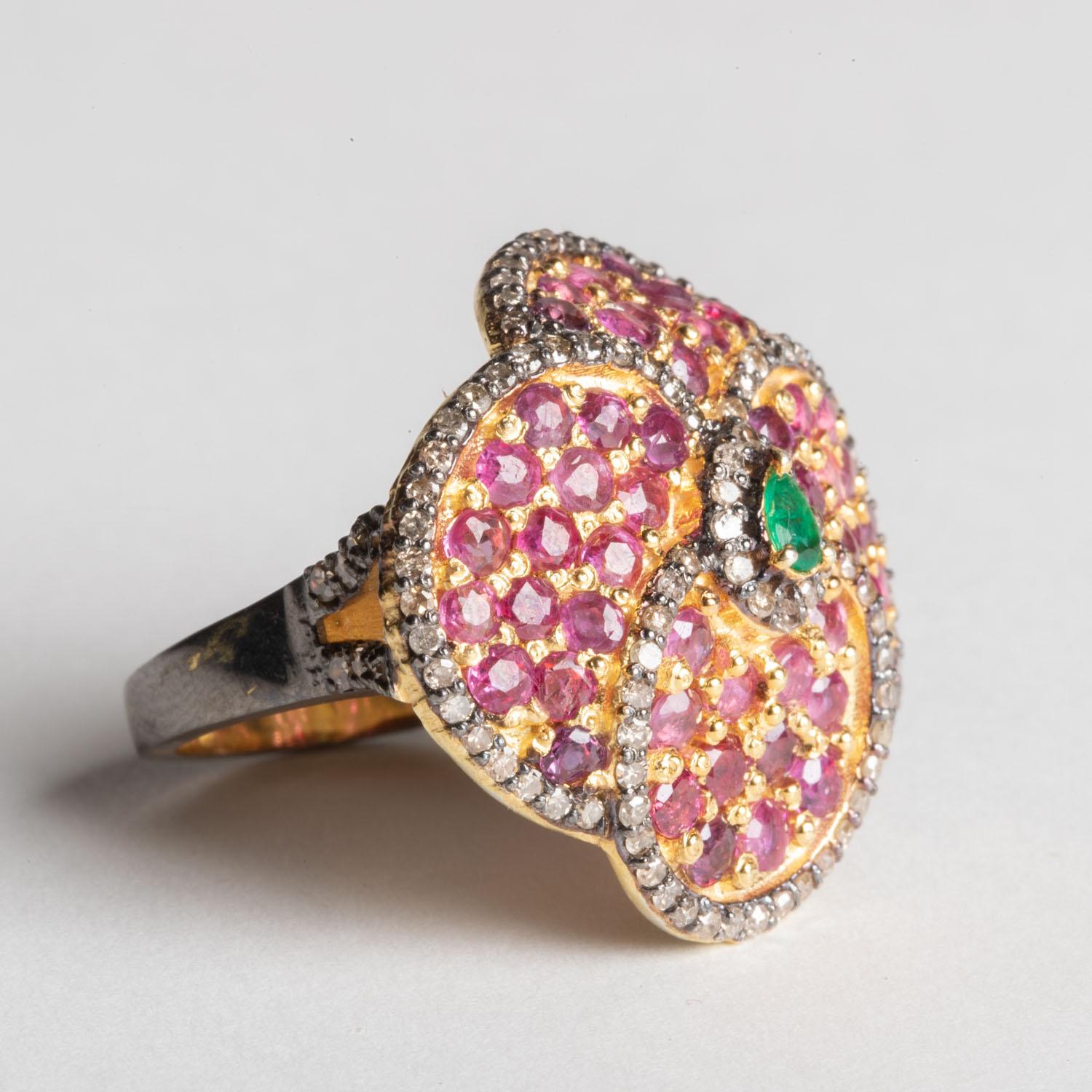 Cette magnifique bague de cocktail à motif de pétales de fleurs est ornée de rubis ronds à facettes, bordés de diamants ronds sertis en pavé et d'une émeraude en forme de poire à facettes au centre.  Des diamants sont également présents le long du