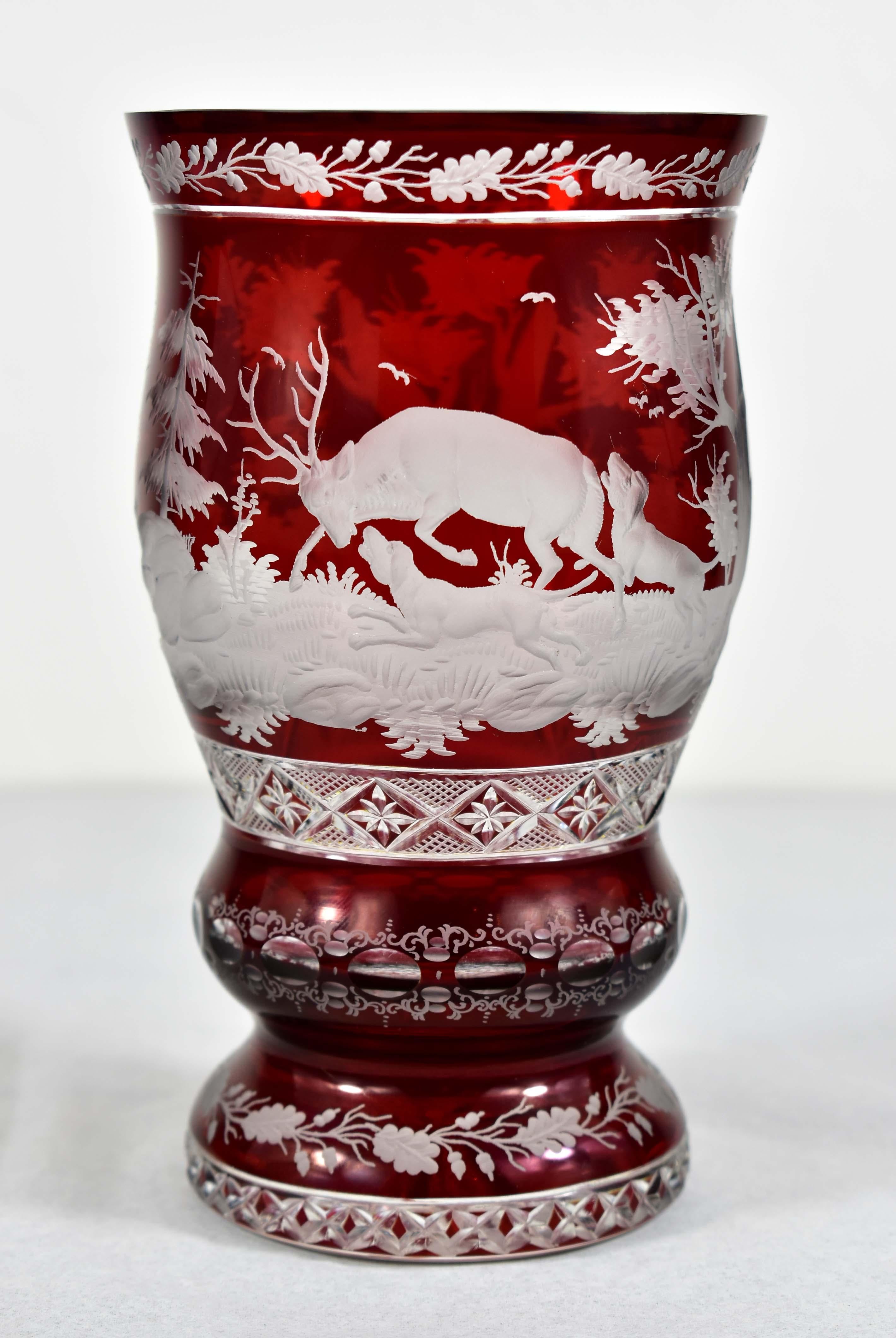 A beautiful cut, engraved and painted goblet made of clear glass with a red lazure. The engraving is a hunting motif of a deer defending against an attack by dogs. In the background is a fleeing hare. Everything is complemented by a beautiful cuting