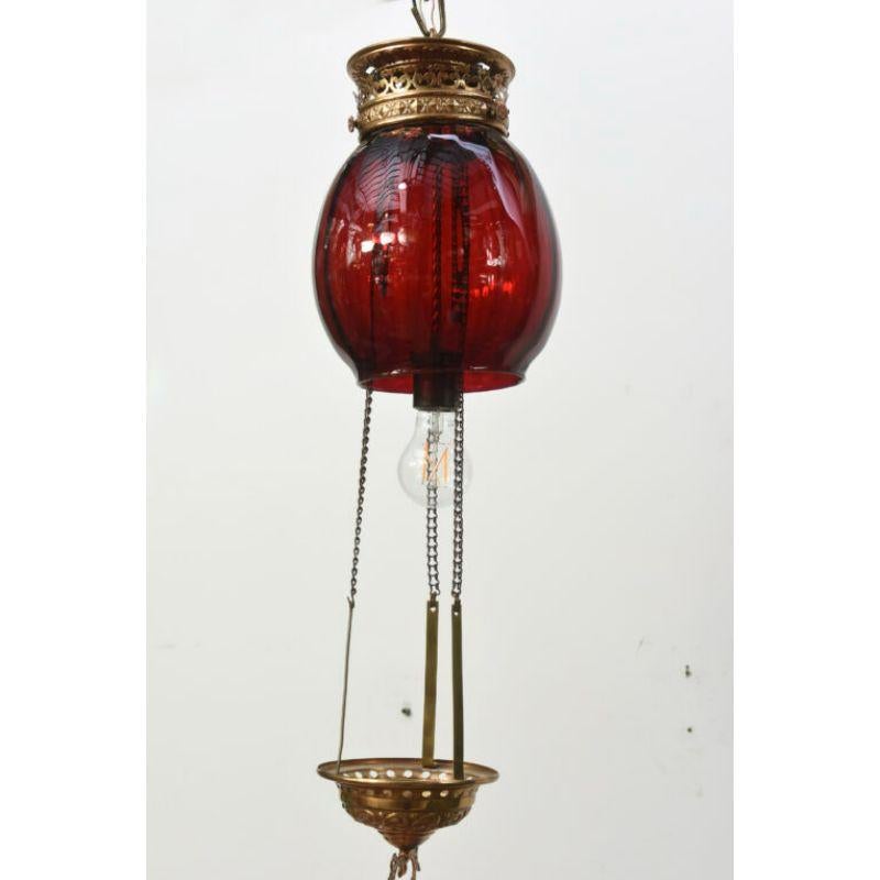 Ruby red electrified oil lantern. Blown red glass globe. The canopy and details are an ornate stamped brass. The restoration included preserving the original pulley system for easy access to the light bulb. Completely restored and rewired. American,