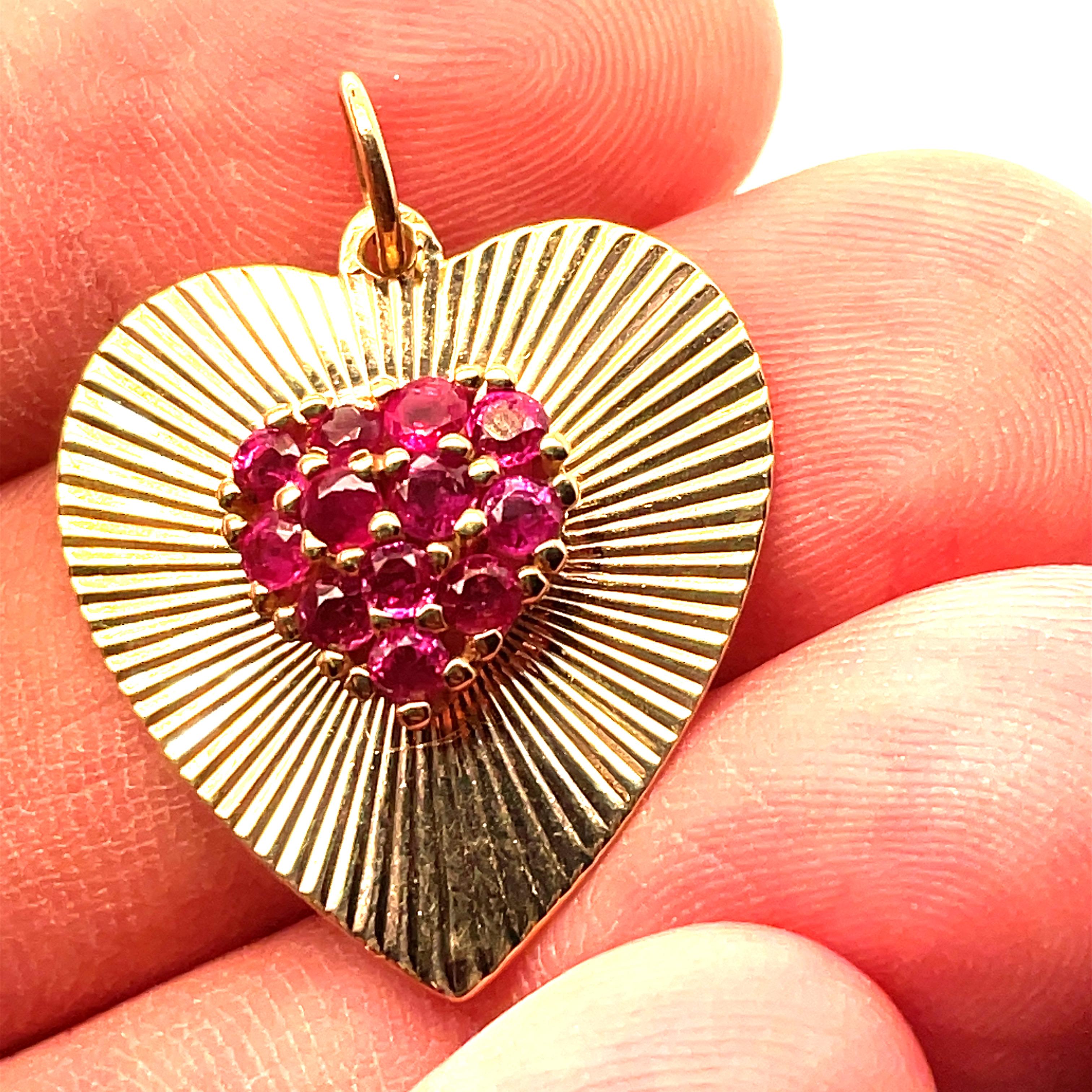 Most appealing figural heart charm./pendant. A figural heart, with a radiating fine line pattern. The center is an applied three-dimensional heart set with bright faceted rubies.  14K yellow gold.  1