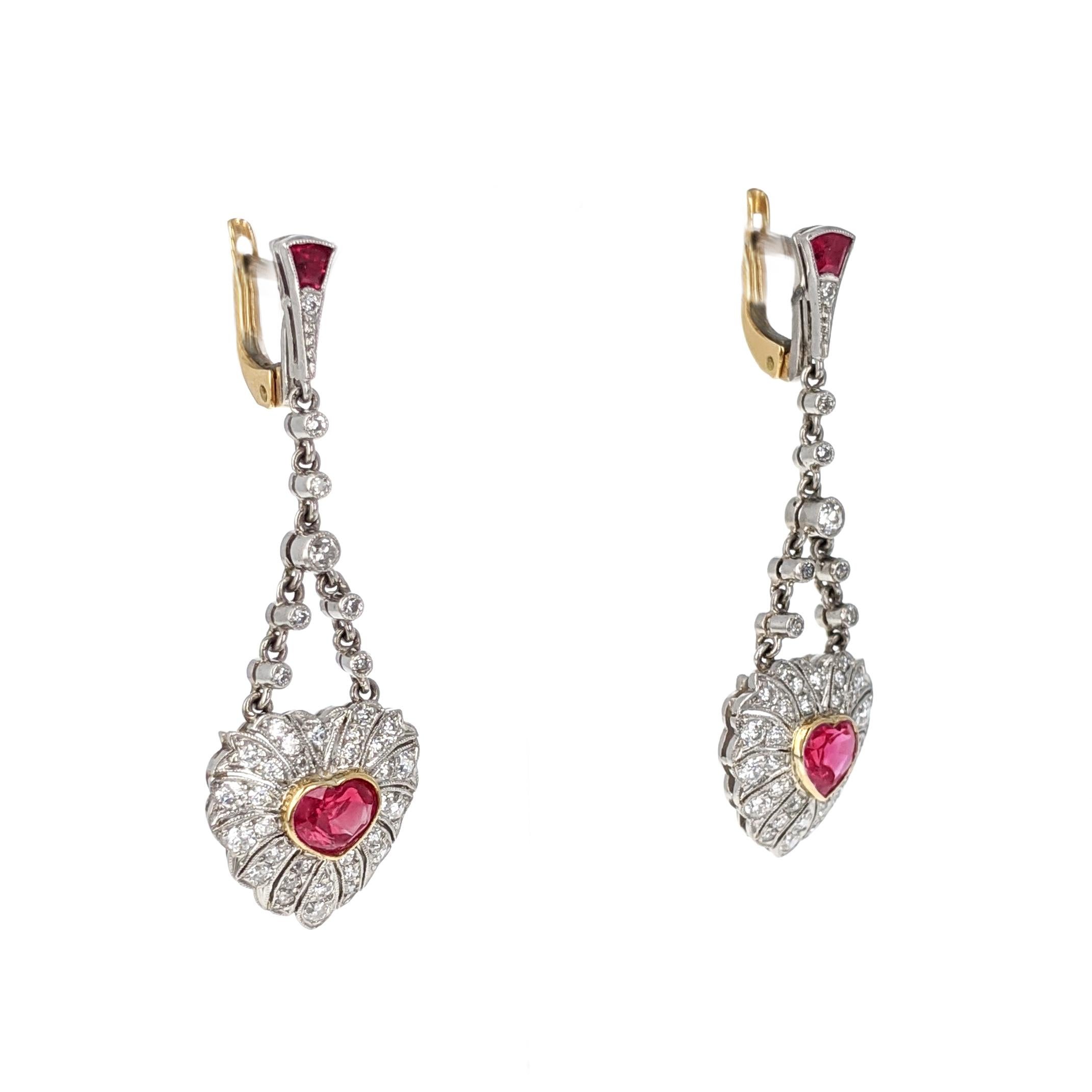 Each of these sweet dangle earrings centers upon a heart shaped ruby, surrounded by single cut diamonds in an openwork design. They are expertly crafted in yellow gold and platinum with delicate milgrain detailing. Each measures approximately 1.5