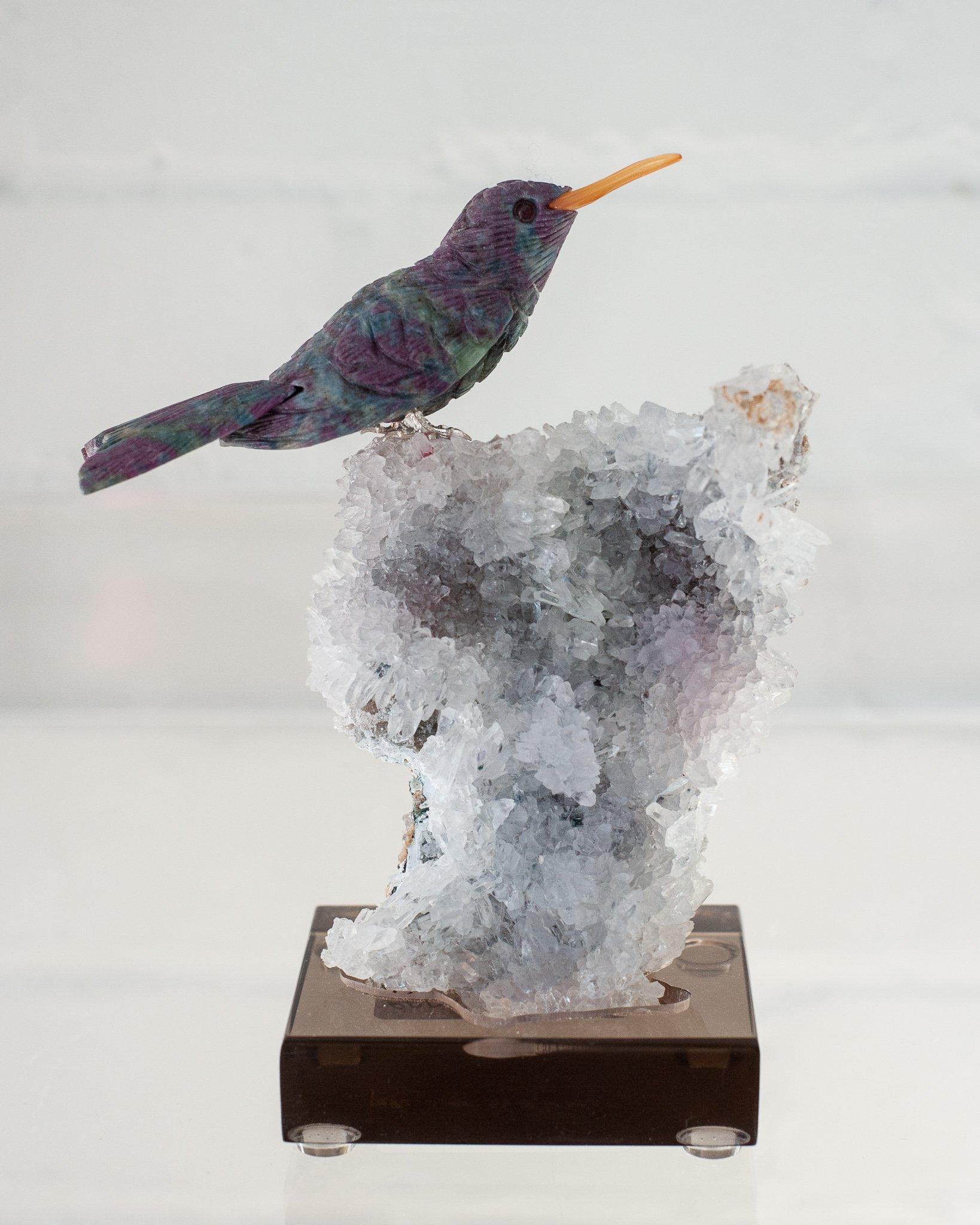 A beautiful hand carved semi precious ruby stone hummingbird mounted on an amethyst and quartz mineral specimen base. This exotic bird is a decorative combination of ornithology and geology.