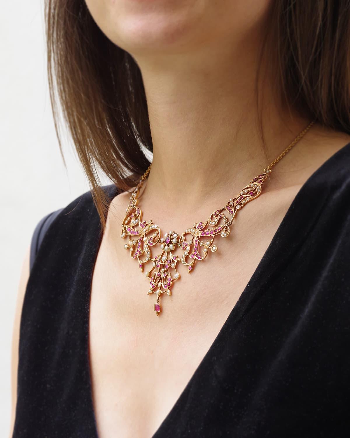 Collana di perle di rubino in oro 18 e 14 carati. Collana composta da cinque piastre traforate con decorazioni floreali e vegetali, interamente incastonate con perle e rubini. Al centro, un rubino ovale da 0,40 carati circondato da perle forma un