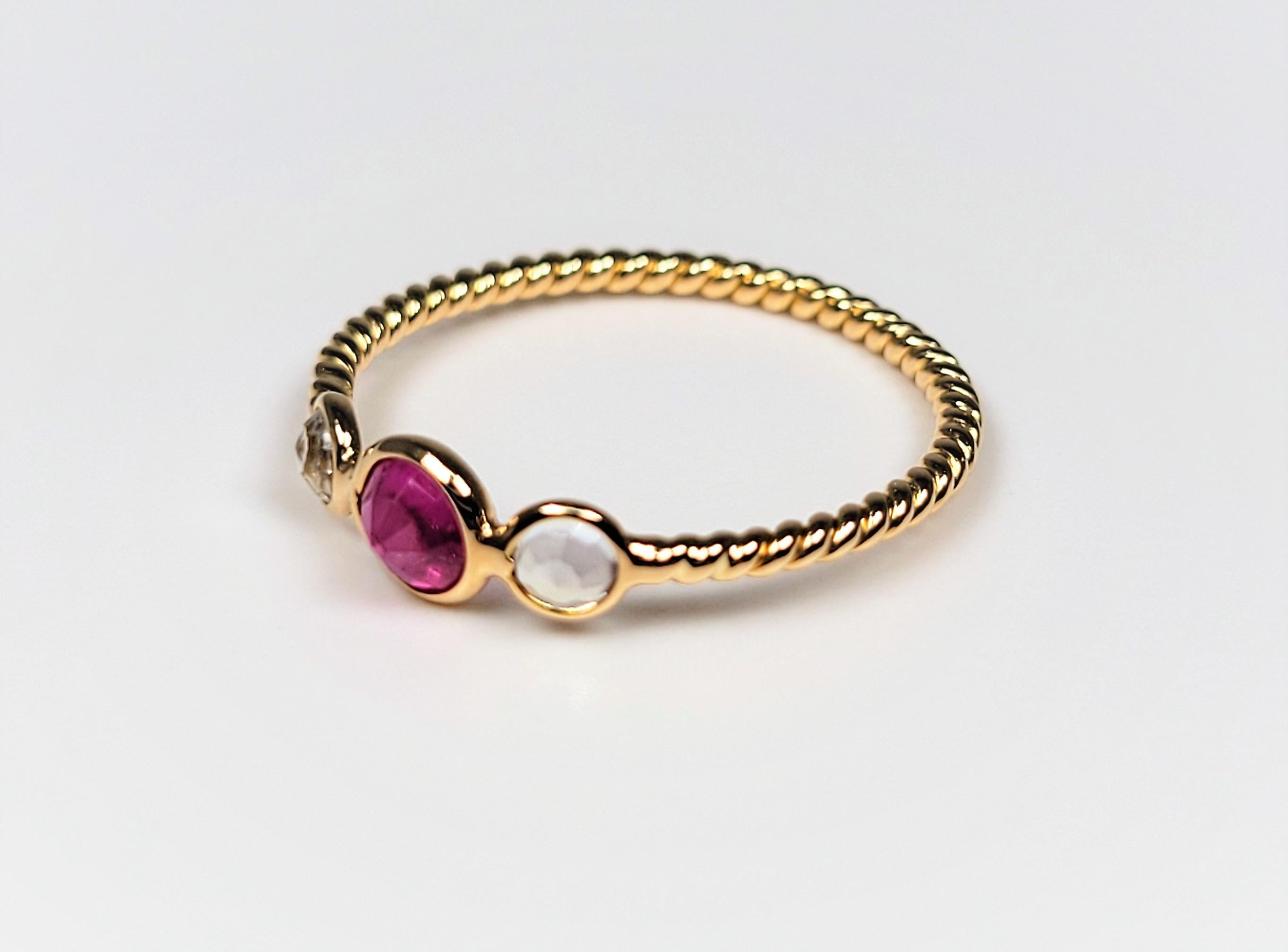 This lovely ring is in 18 karat yellow gold and supports an inverted round ruby, flanked by two bezel-set, inverted, round rainbow moonstones. 