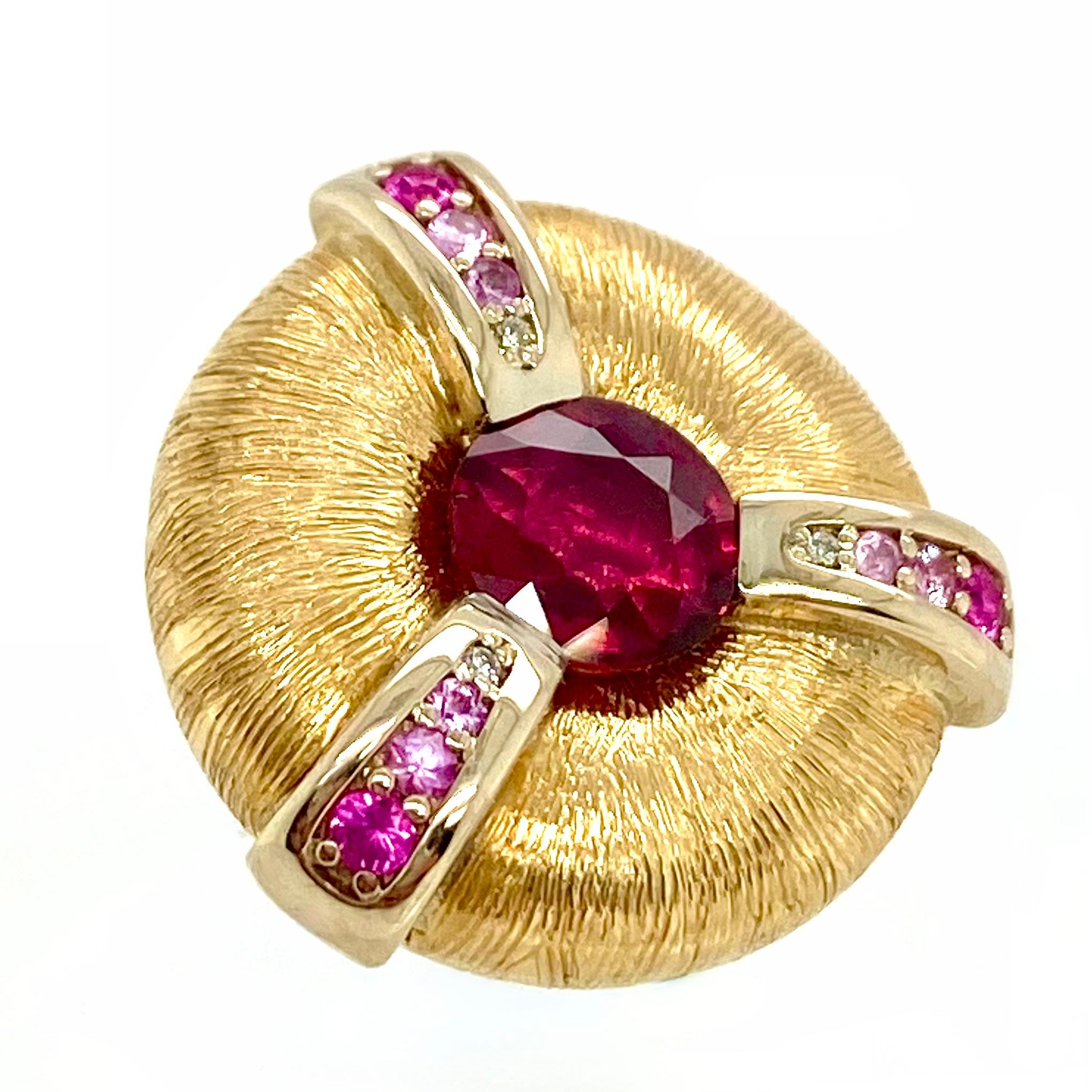This one-of-a-kind Ruby ring in 18k yellow features a doughnut shaped top that holds the ruby in its center. Three 18k white gold bands spread out from the ruby towards the outer edge of the top. These bands are set with pink sapphires whose colors