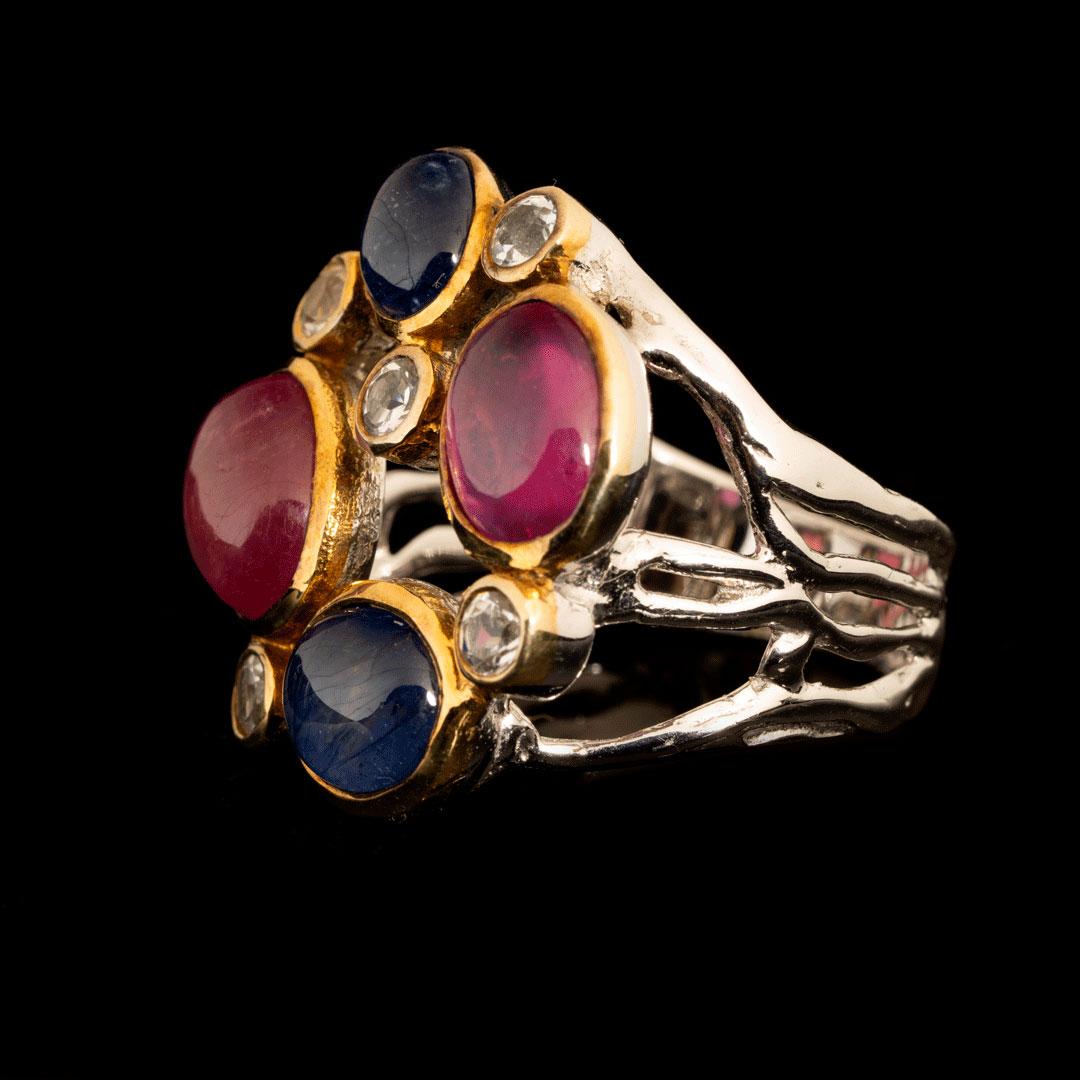 This handsome ring features polished deep blue sapphire and ruby cabochons set off by sparkling faceted white topaz stones for a lush bauble sure to turn heads. This sophisticated stunner is perfect for the holiday season and all through the rest of