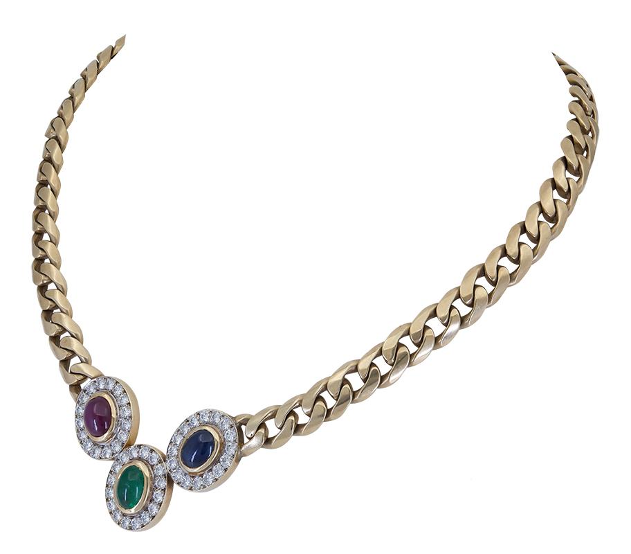 A unique piece of jewelry showcasing a pendant with a cabochon ruby, sapphire, and emerald, creating a stunning trinity design. Each precious gemstone is bezel set and surrounded by round brilliant diamonds. Pendant Suspended on a cuban link chain