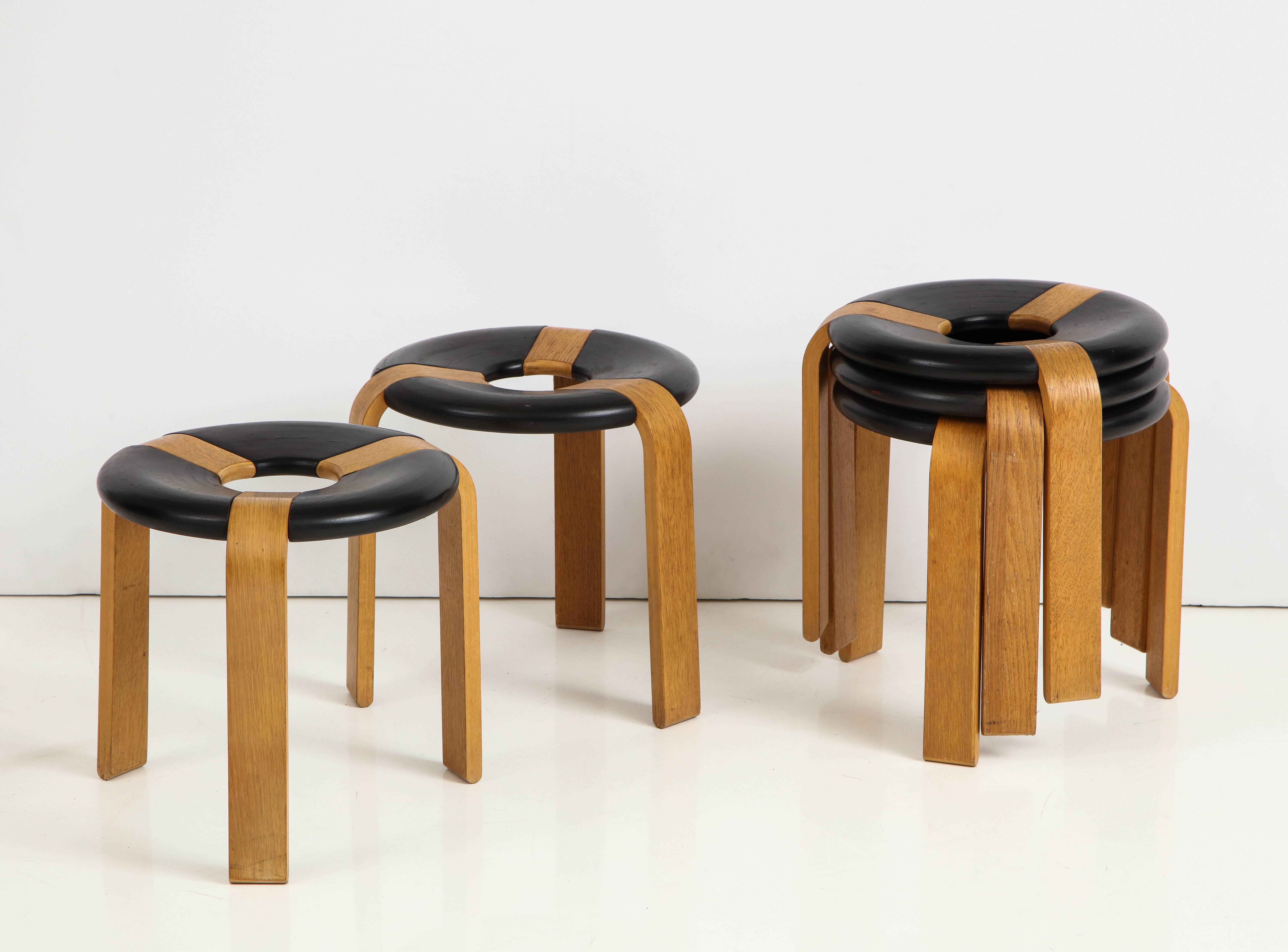 Set of five stacking stools in oak plywood and lacquered plywood. By Rud Thygesen and Johnny Sorensen for Magnus Olesen A/S, Denmark, circa 1970s. A distinctive design wherein the three bent plywood legs culminate at the center of a donut-shaped
