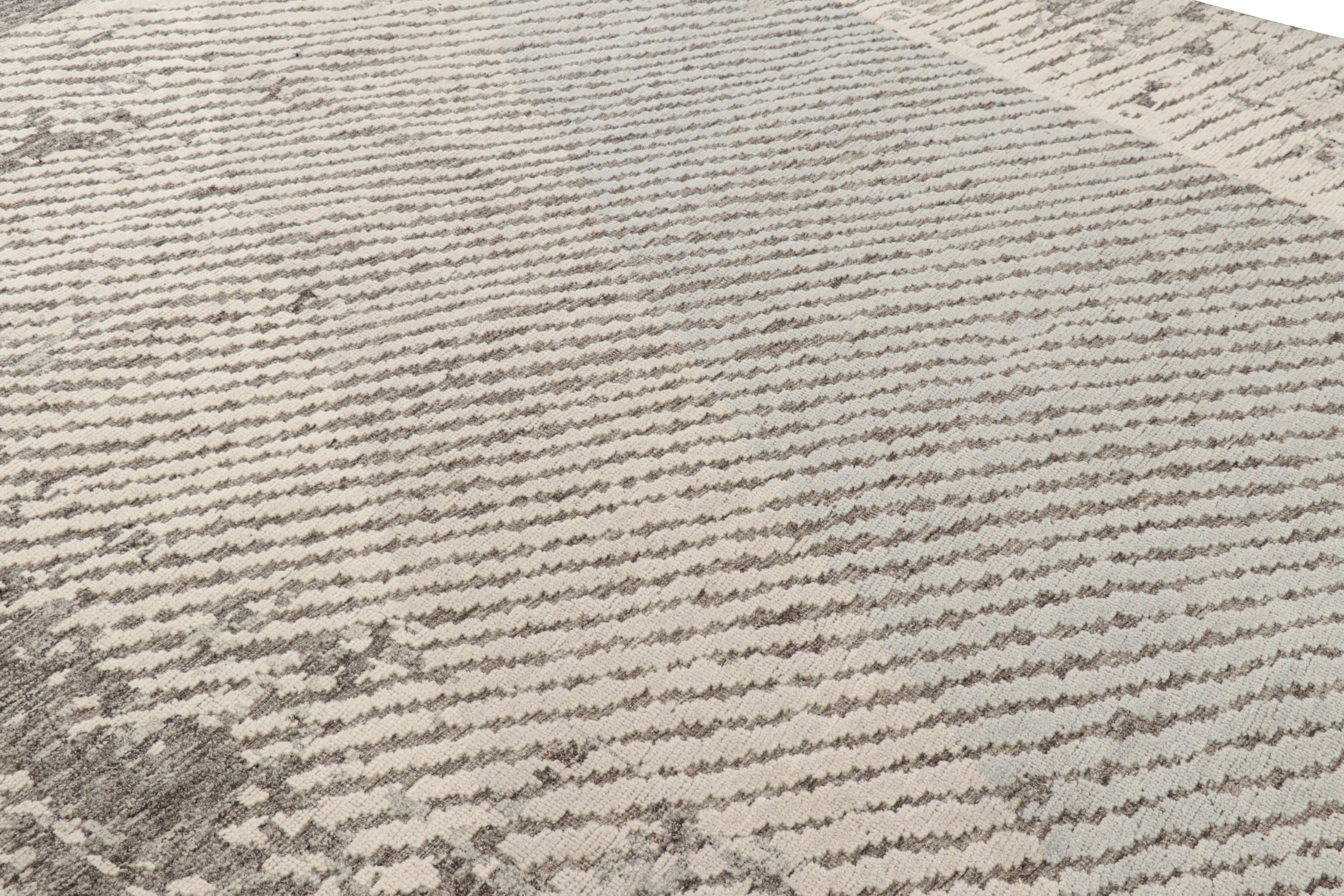 Dieser moderne, abstrakte Teppich im Format 5 x 6 ist aus Wolle handgeknüpft. Graue, blaue und cremeweiße Töne unterstreichen geometrische Muster, die an malerische Pinselstriche erinnern, in Verbindung mit einer Hoch-Tief-Struktur. 

Über das