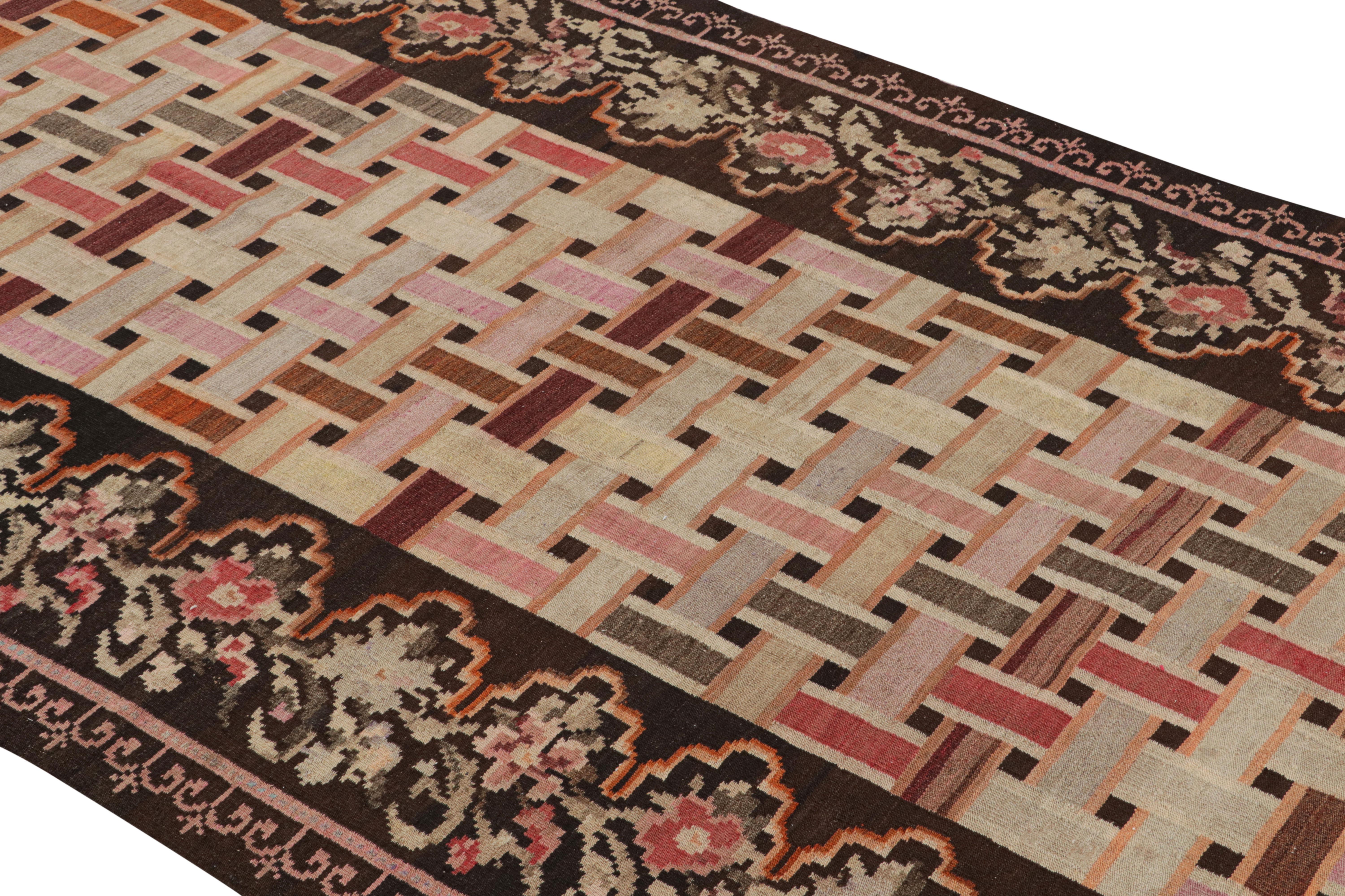 Handwoven in a wool flat-weave originating from Turkey circa 1950-1960, this vintage Kilim rug connotes a midcentury Bessarabian Kilim rug design in a play of rich Classic brown with European style pink, beige, and varied accenting hues in the
