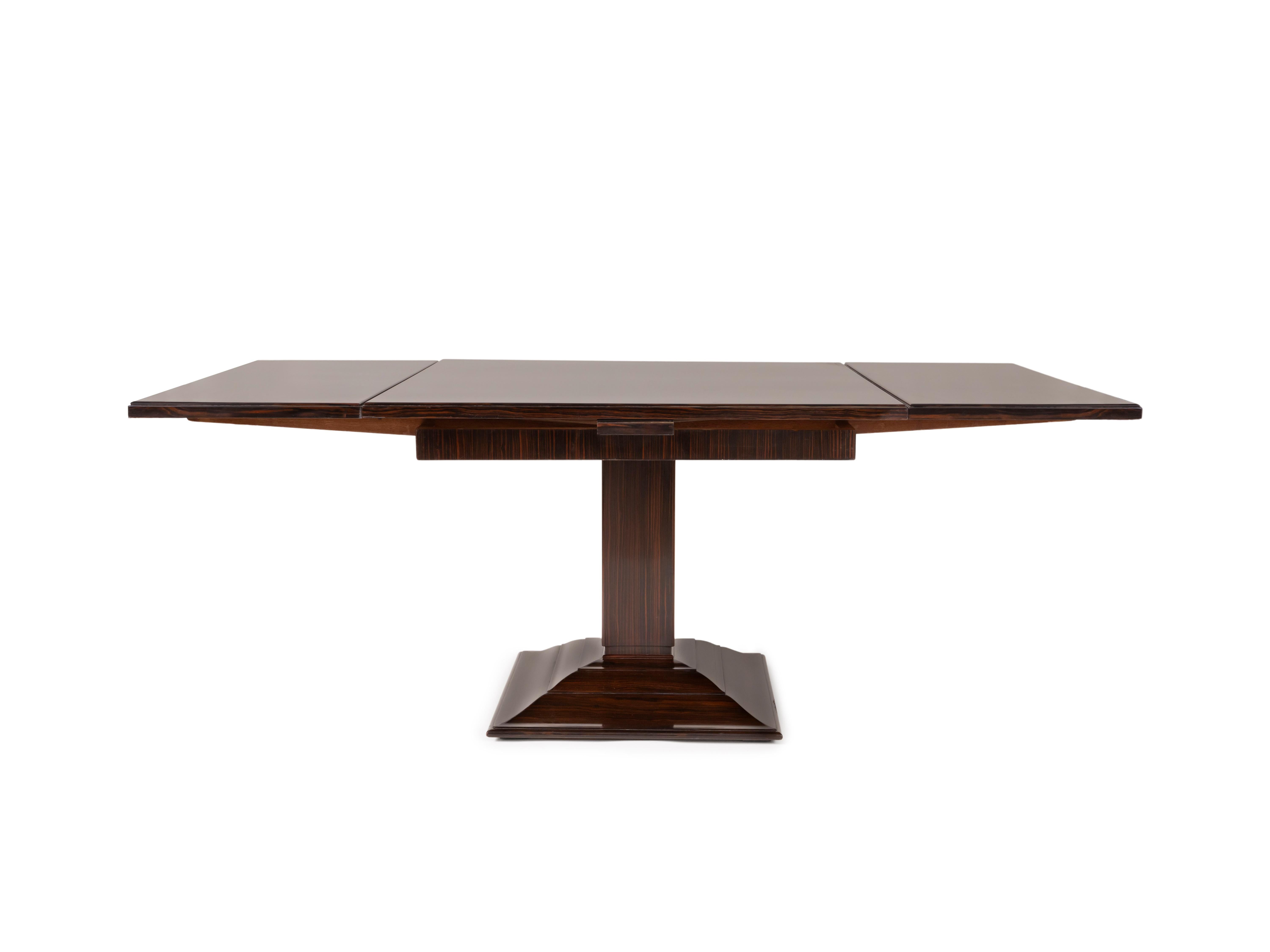 Dining table in Macassar ebony and Macassar ebony veneer on a Hungarian oak frame, with a square top and two Italian-style extension leaves. The central pedestal rests on a square cavetto-moulded base. Referenced under no. 1315NR in the Ruhlmann