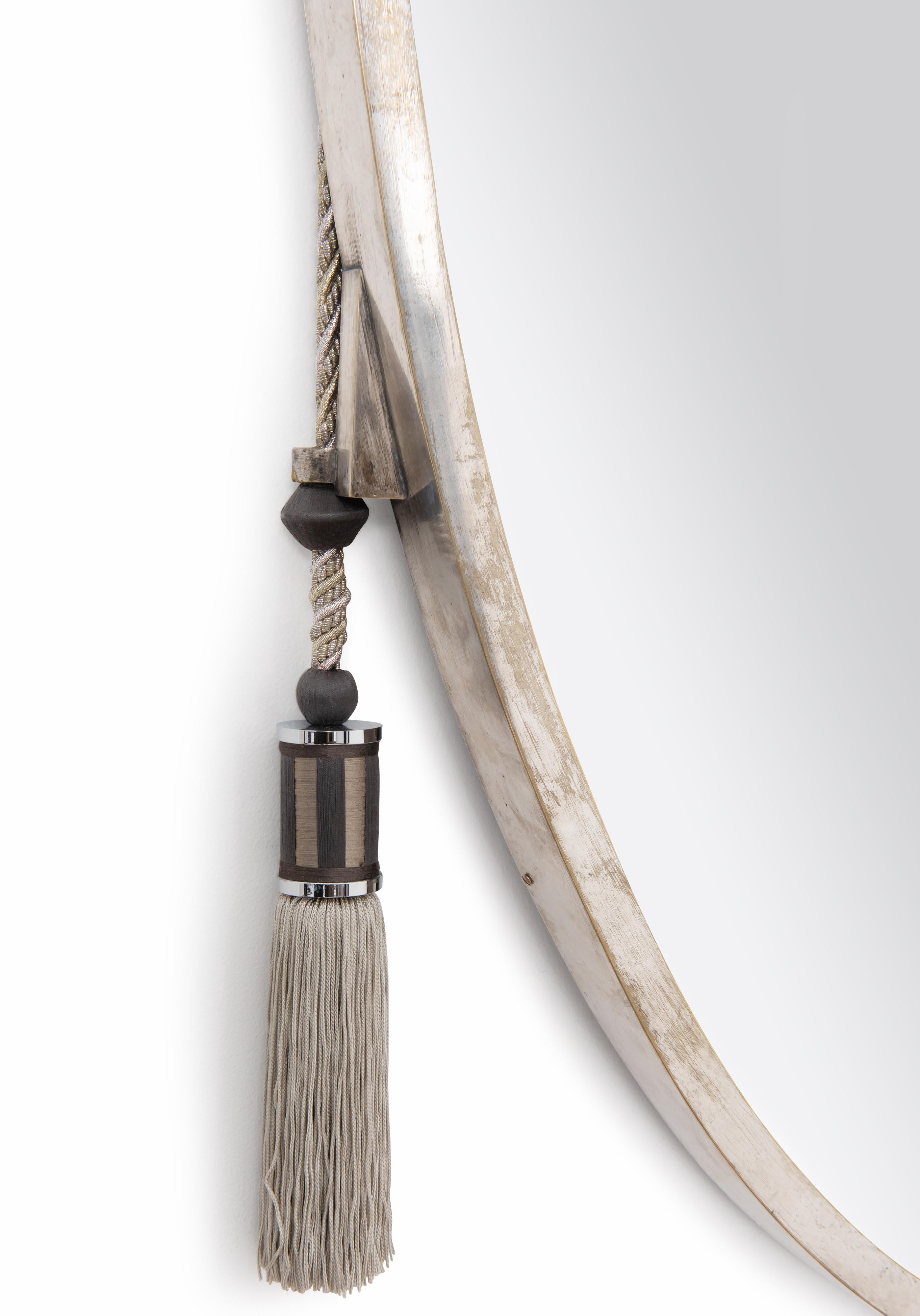 Miroir ovale à suspendre avec cadre en bronze argenté, orné sur sa partie médiane de deux œillets destinés à recevoir des garnitures en soie. Miroir avec bord biseauté et dos plaqué acajou.  Estampillé 