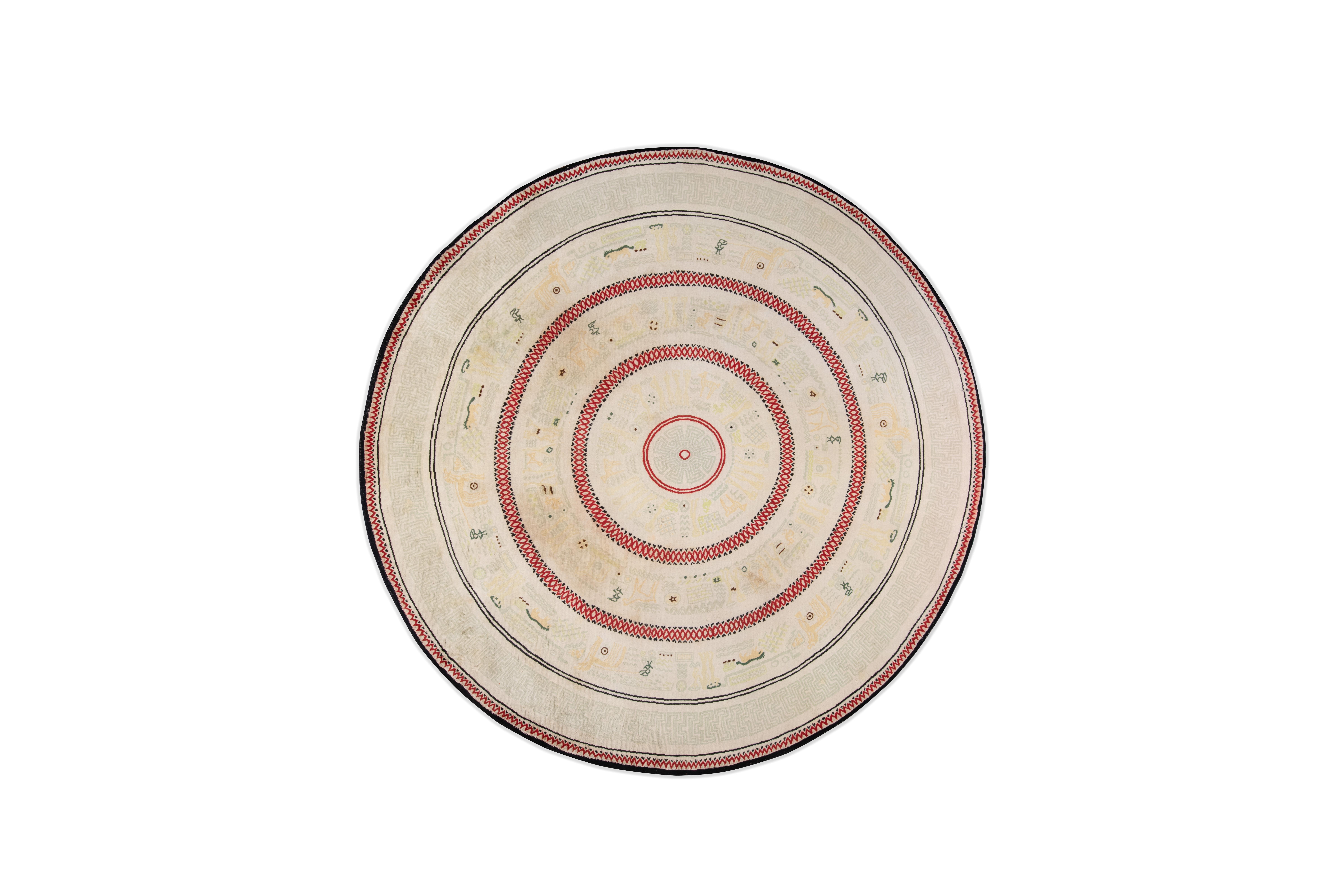 Important tapis circulaire en laine à décor concentrique de frises géométriques rouges et noires formées de pictogrammes ainsi que d'idéogrammes aztèques jaunes et gris sur fond crème conçu par  'Émile-Jacques Ruhlmann et produit par Alfred