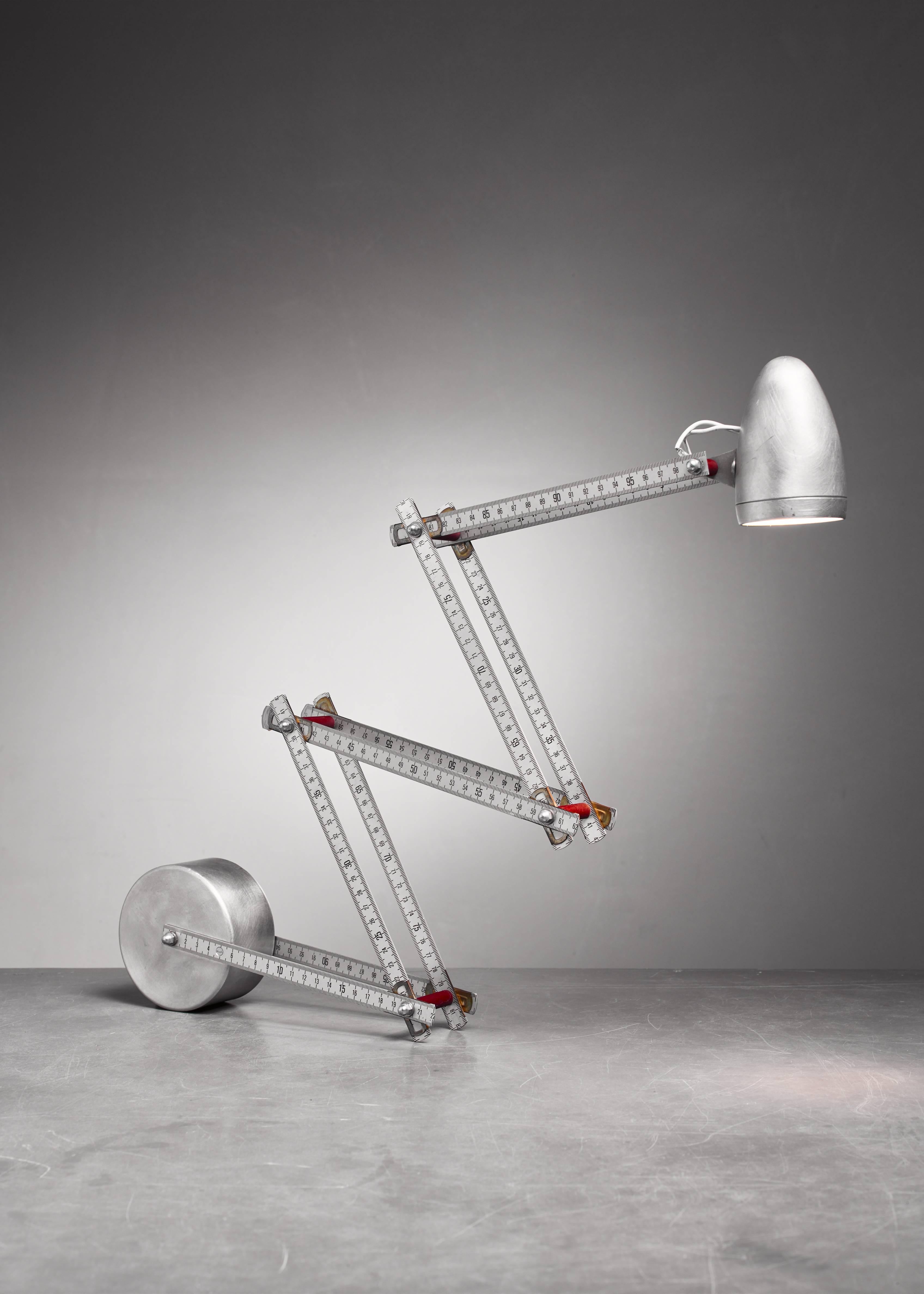 A very interesting, engineered aluminum French table lamp constructed out of two folding rulers, with a wheel as base.
Height adjustable from circa 20 to 90 (8 to 35 inch) and the shade is also adjustable. Due to its many joints it can be placed in