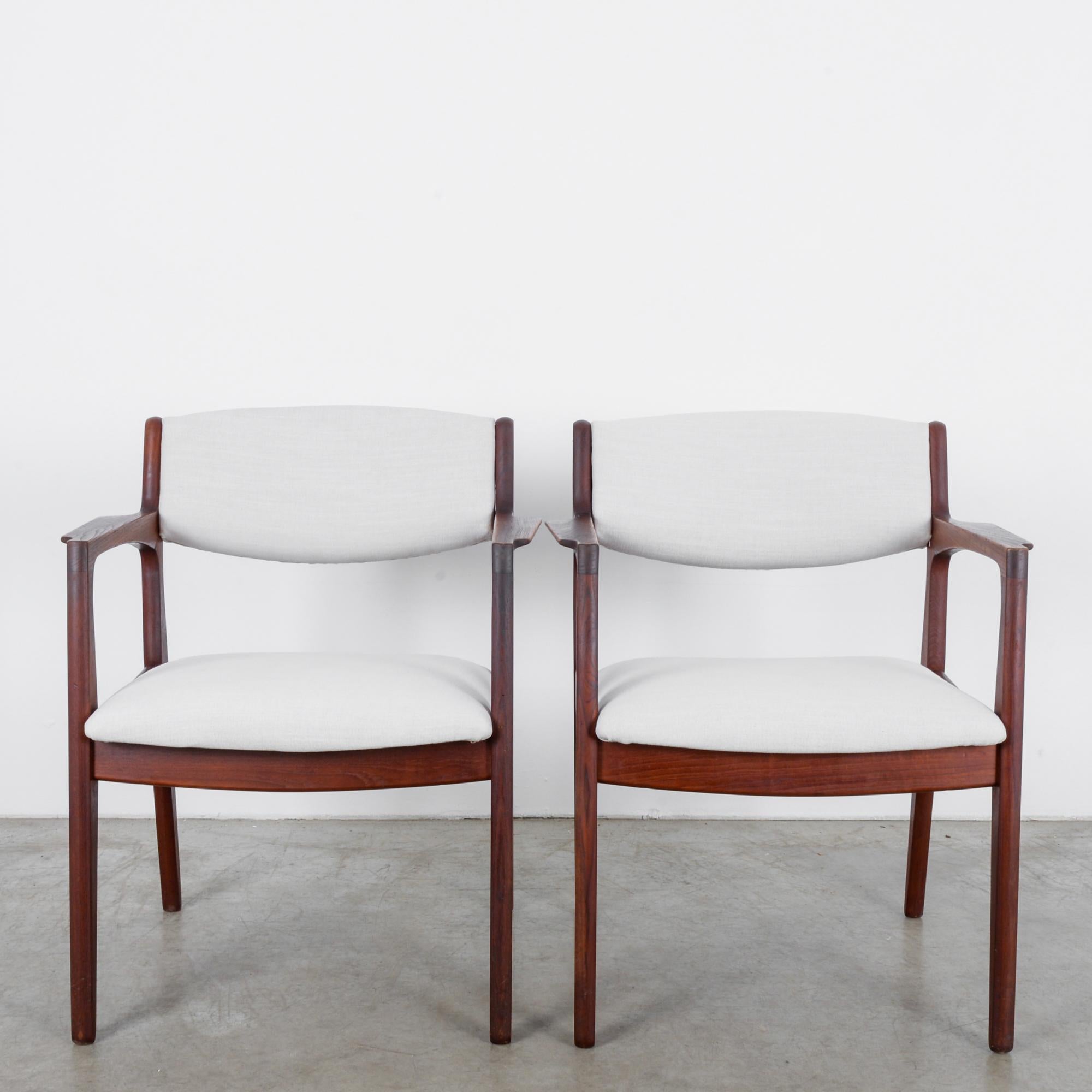This pair of teak armchairs was made by Ørum Møbler in Denmark, circa 1960 and offer both comfort and style. The subtle curves in the tapered legs and armrests give these chairs an air of refinement. Ivory white upholstered seats and backs highlight