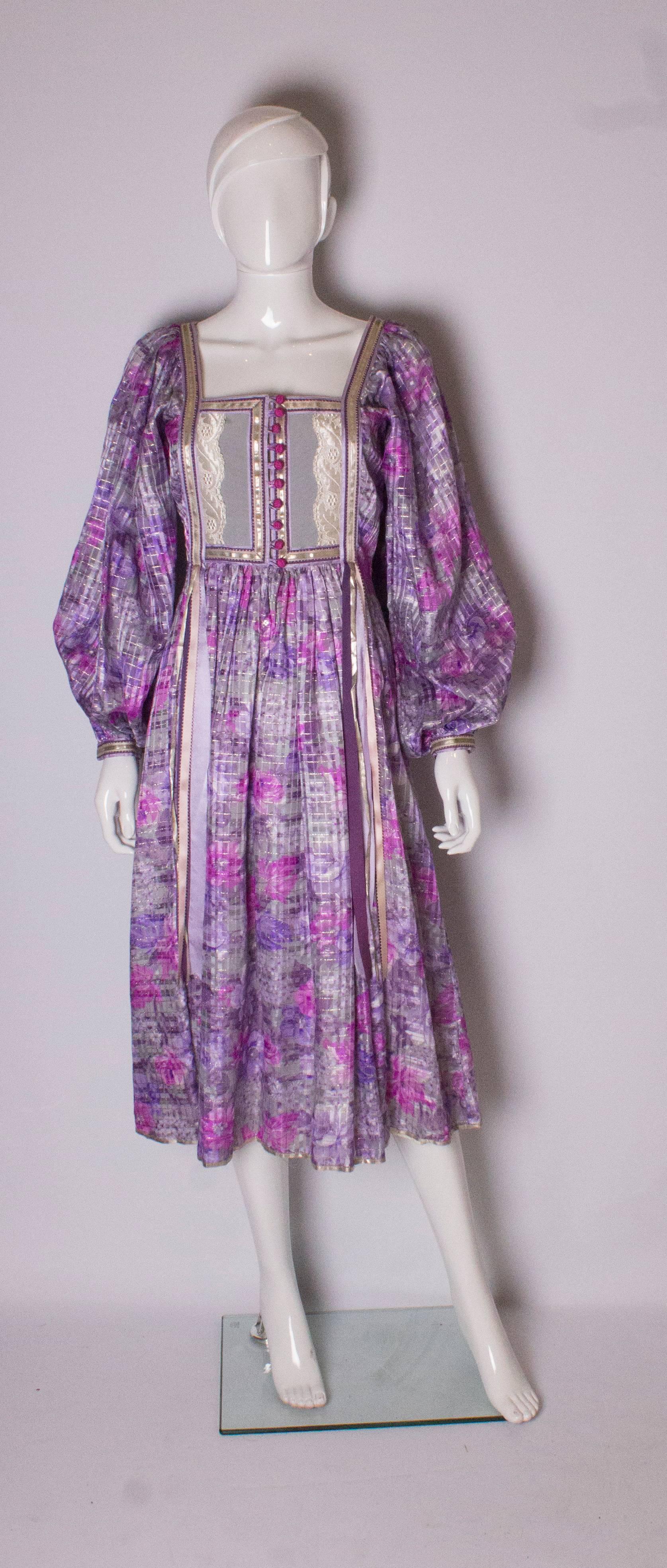 A pretty 70s dress by Rumak, in a lilac and grey silk chiffon with gold thread running through. The dress has a square neckline at the front and back with ribbon detail, and puff sleeves.
