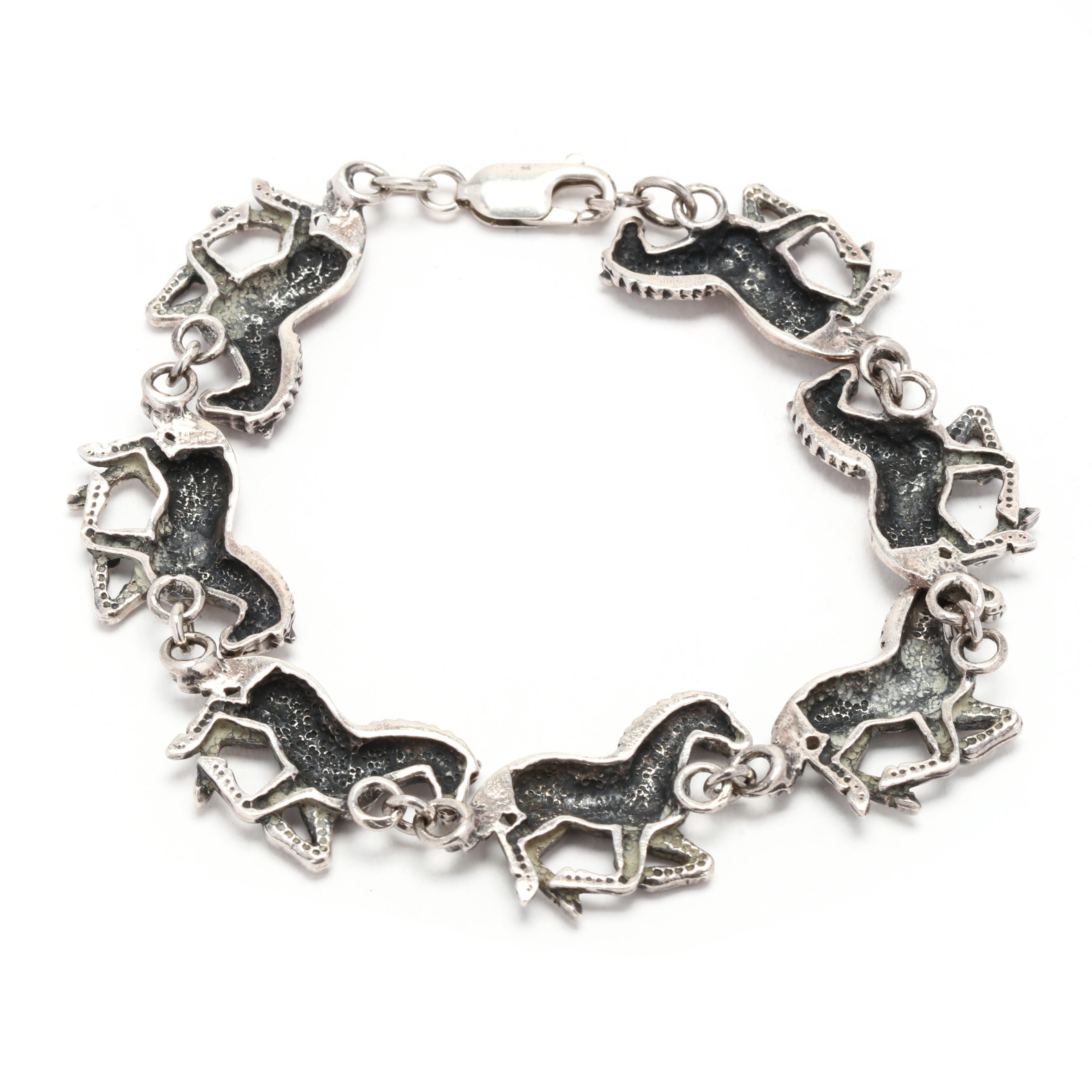 Ein Armband aus Sterlingsilber mit einem laufenden Pferd.  Dieses Armband mit Pferdemotiv besteht aus sieben Gliedern, die jeweils ein laufendes Pferd darstellen und mit einem Karabinerverschluss verschlossen werden.  Er ist mit 925