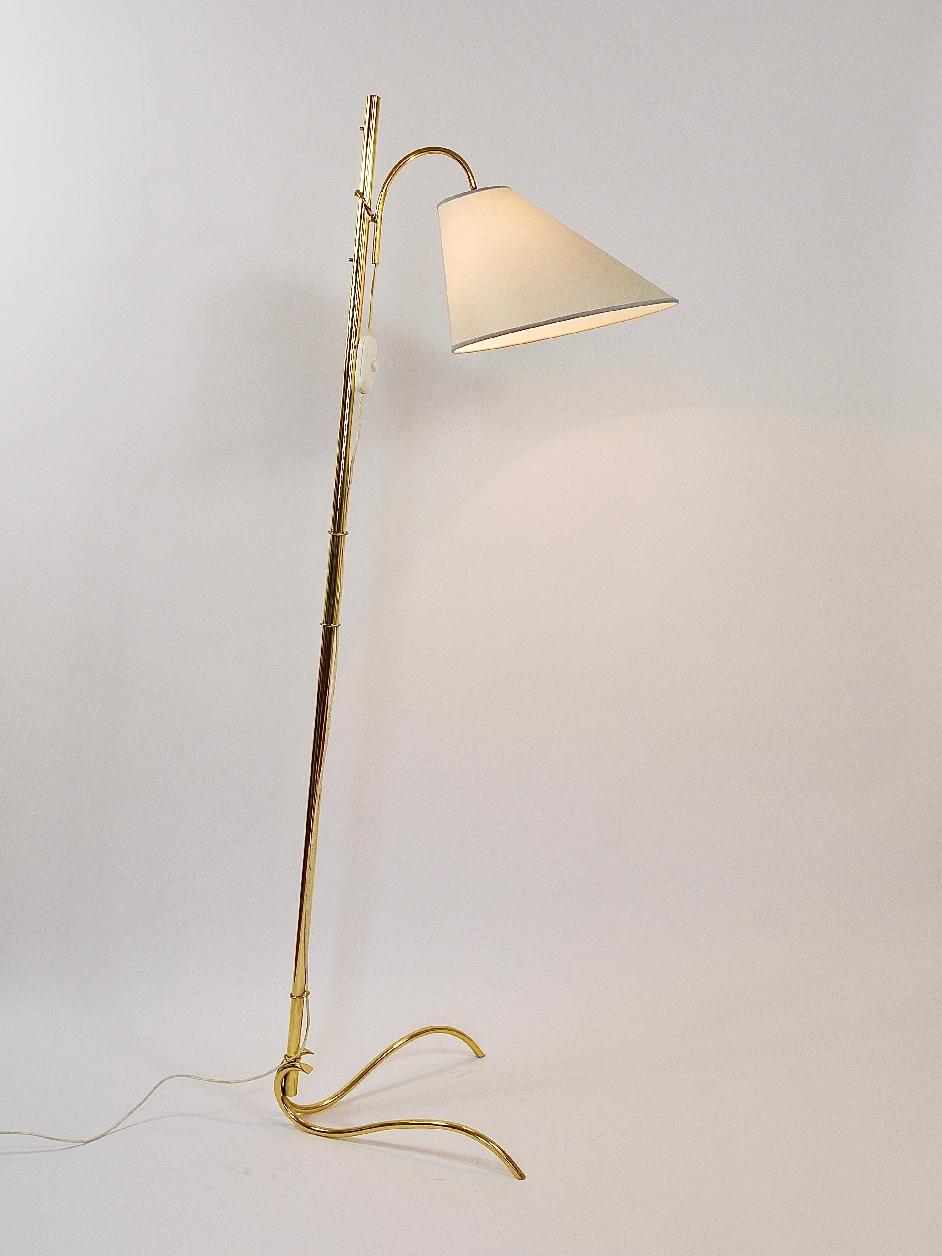 A delicate and elegant Mid-Century floor lamp from the 1950s, designed and executed by Rupert Nikoll in Vienna, Austria. The lamp is made of brass and features a lovely curved brass base. Its lampshade has an unusual conical yet asymmetrical shape.