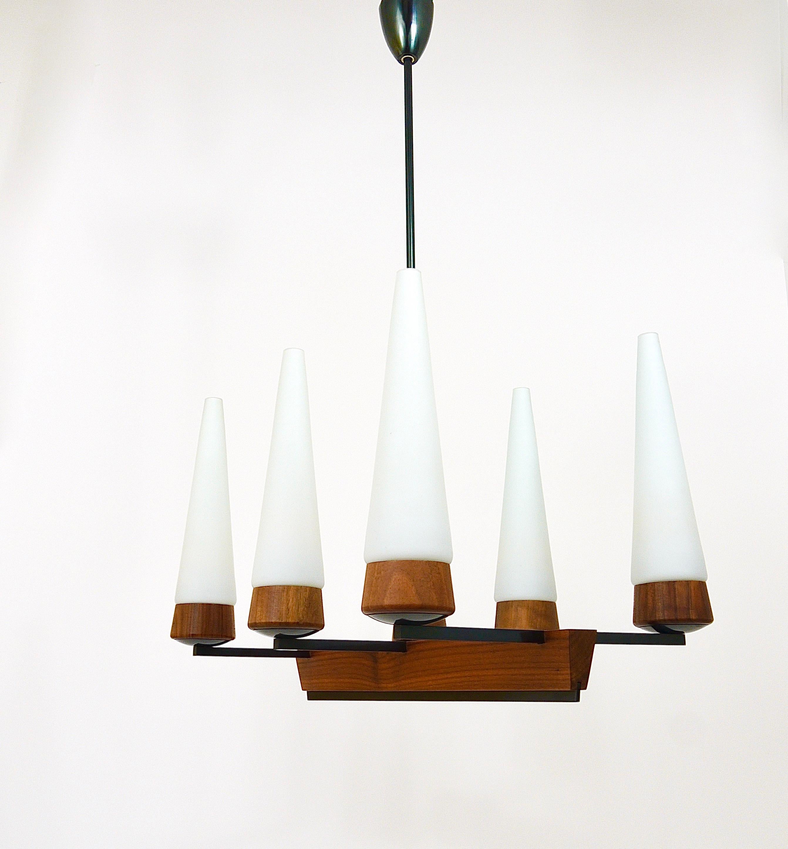 A beautiful and elegant Scandinavian style Midcentury chandelier from the 1950s. Executed by Rupert Nikoll, Vienna, Austria. The chandelier is made of dark-brown wood and black-finished brass. It has 6 arms with conical white satined opal glass