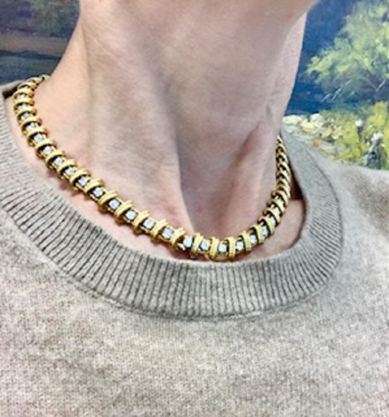 This vintage Ruser diamond necklace is crafted from 18k yellow gold and set with round diamonds in a repeating geometric pattern. Each diamond is framed by a textured gold border, creating an angular motif throughout the length of the necklace. The