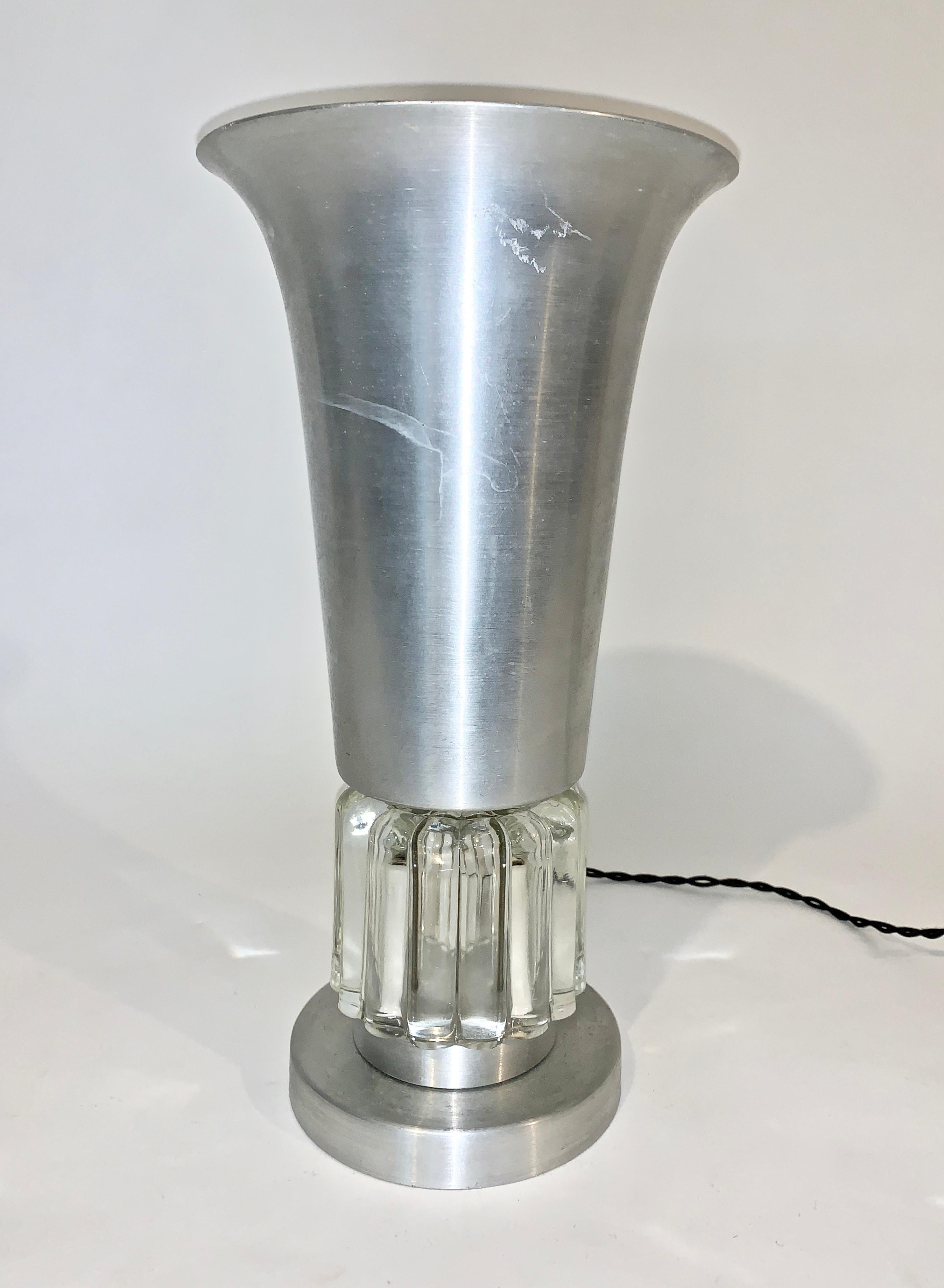 Art Deco brushed aluminum and clear glass table lamp, up light attributed to Russel Wright. Featuring a cast aluminum bell shade and round base with transparent ribbed glass detail. 