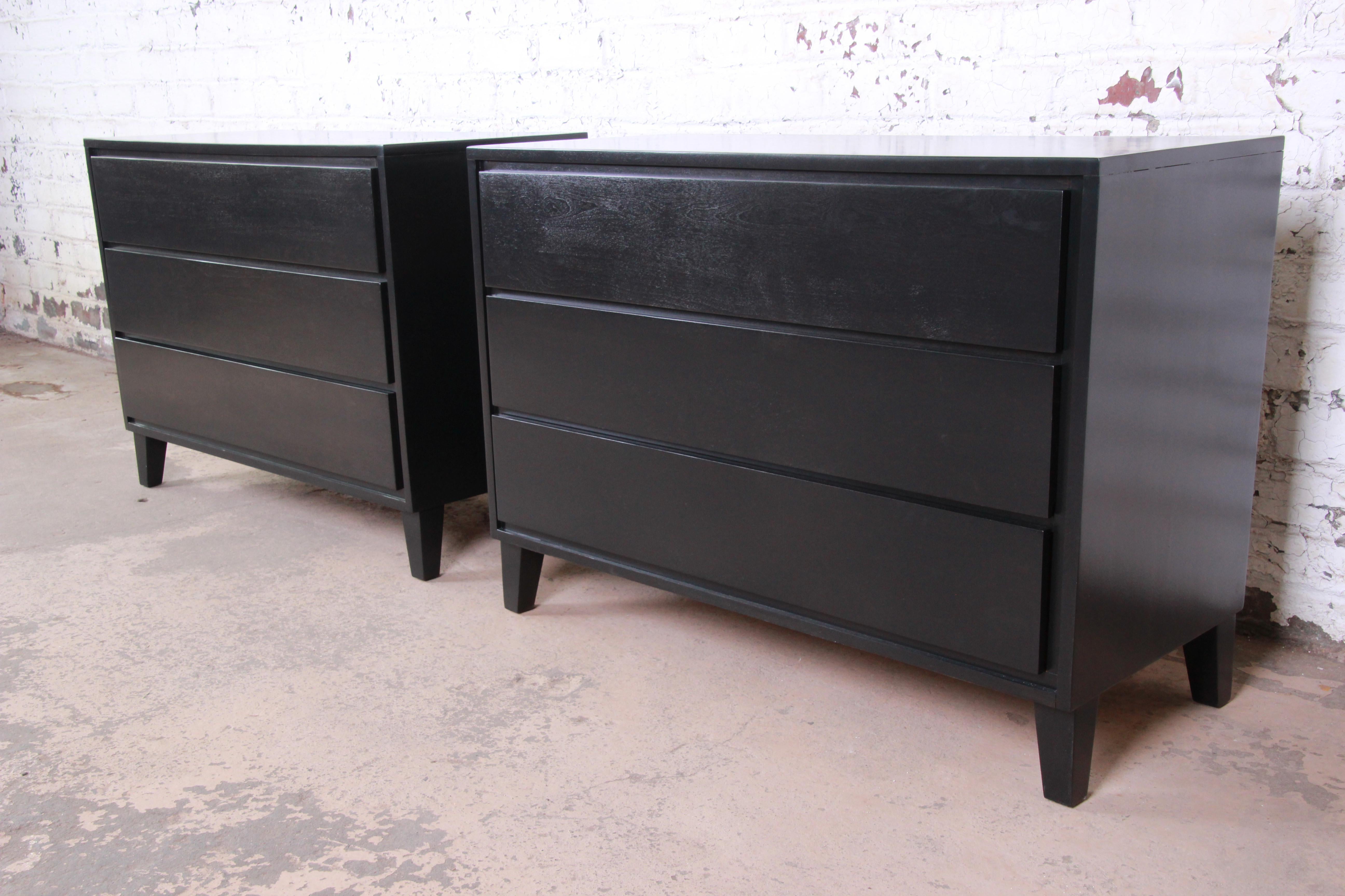 An exceptional pair of ebonized three-drawer dressers or bedside chests designed by Russel Wright for his American Modern line for Conant Ball. The chests features solid birch wood construction, with sleek, Minimalist Mid-Century Modern design. They