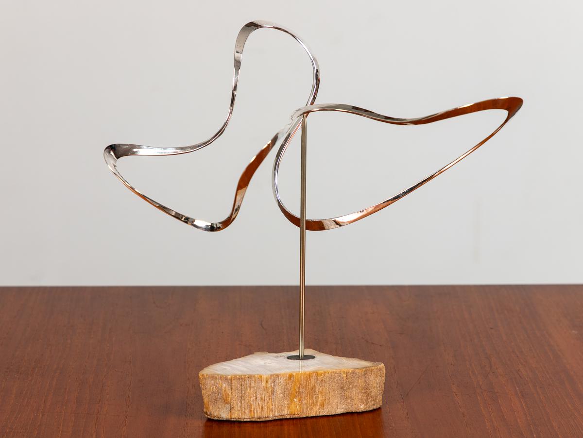 Abstract modernist sculpture, created by Russell Secrest. Drawing on his background in jewelry, the metal artist creates a dynamic form, in elegant hammered silver. The sculpture rotates on a polished steel rod, on a stone base, and is beautiful at