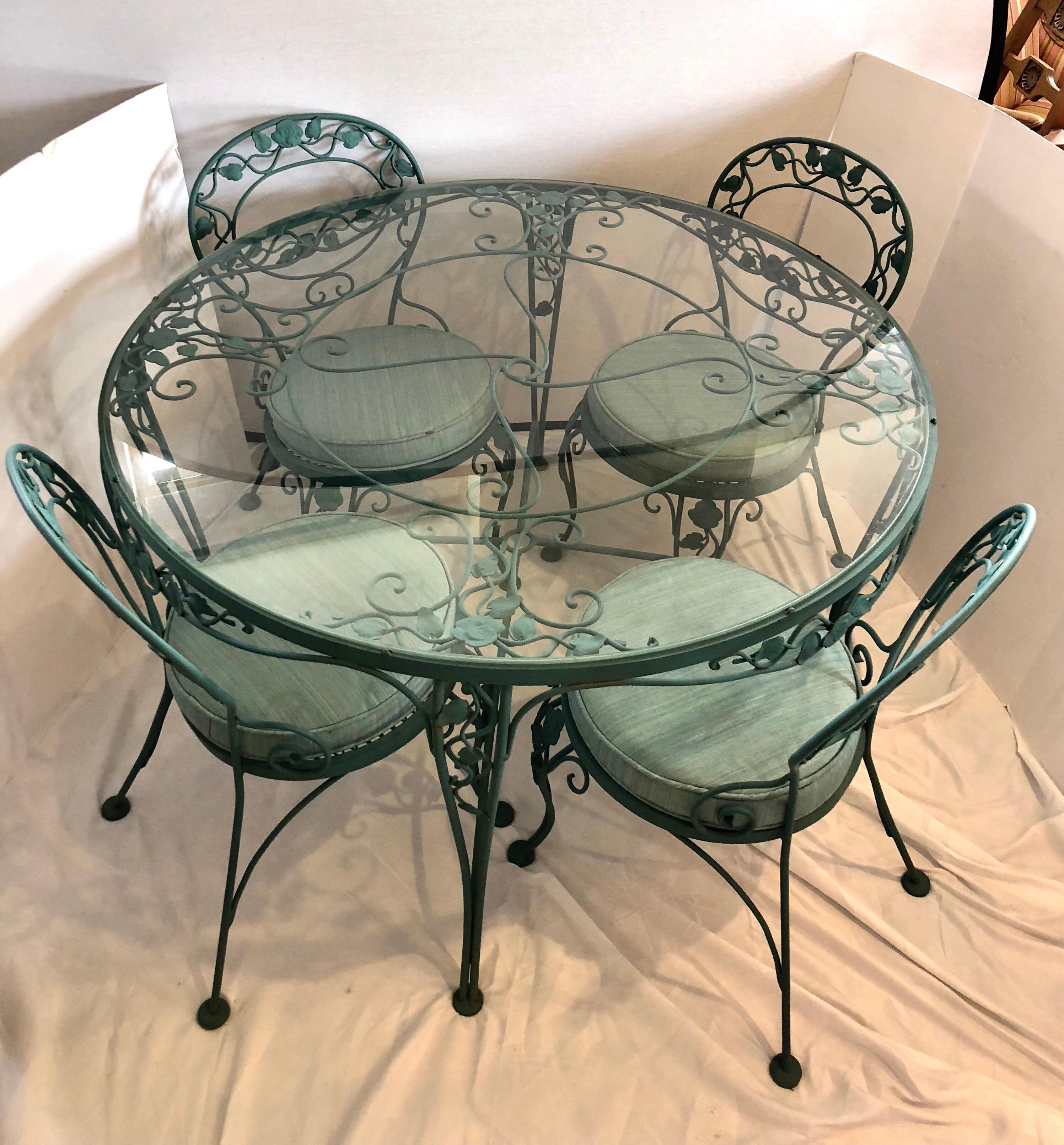 Classic signed Russell Woodard wrought iron patio set with intricate metalwork throughout.
Features fitted glass top that sits on floral metalwork.