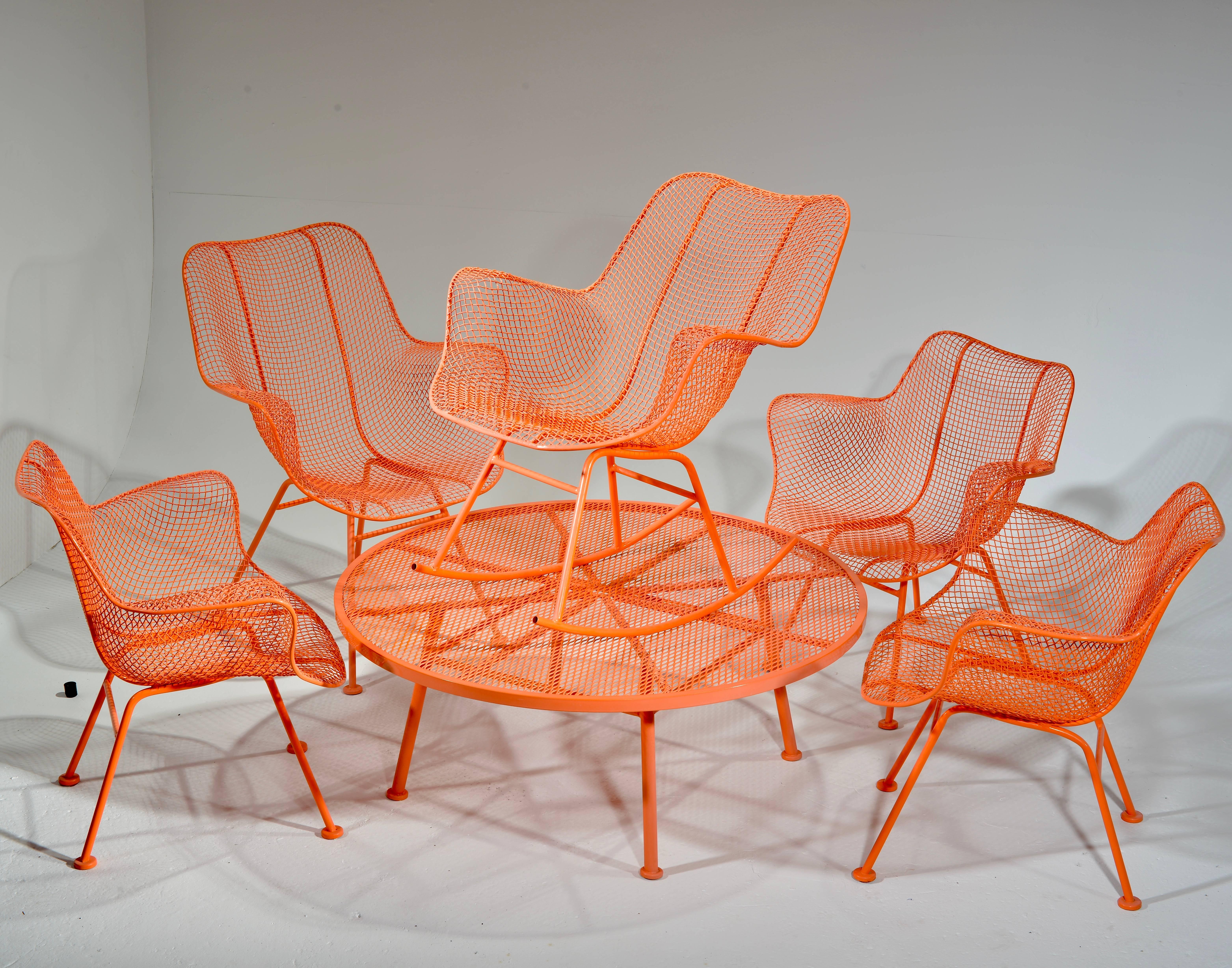A unique set of six 1950s wrought iron chairs and table from Russell Woodard's Sculptura collection. Includes one round coffee table, three armed lounge chairs, one armed side chair, and one rocking chair. This set has been powder coated in salmon