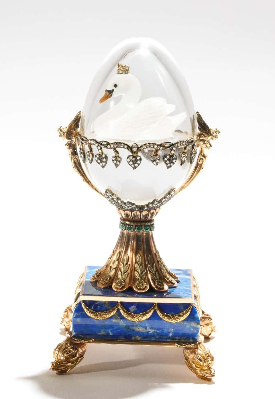 A beautiful Russian 14- karat gold, diamonds, emeralds, lapis lazuli and glass egg with swan, by S. Rudle, 20th century.  

Two color, 14-karat gold mounts, the egg in the Faberge style with a floating frosted glass swan, mounted with diamonds,