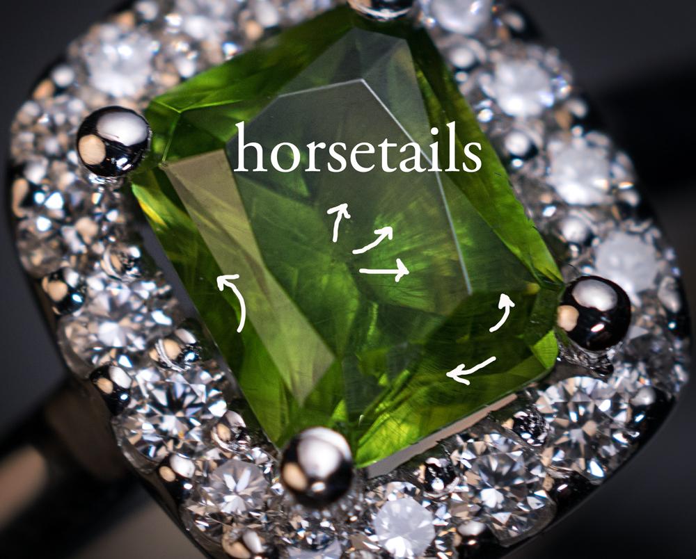 This contemporary 14K white gold ring features a 1.45 ct radiant cut Russian demantoid of a lime green color framed by bright white diamonds. This is a very unusual cut for demantoids. The stone features some fine “horsetail” inclusions which are