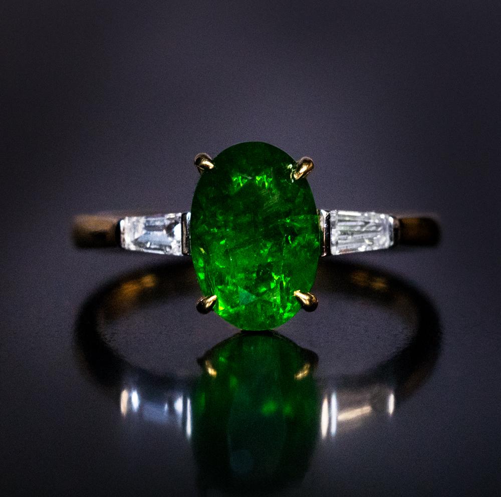 This contemporary gold engagement ring features a 2.33 ct old mine cut Russian demantoid from the early 1900s of a deep green color. The center stone is flanked by a pair of tapered baguette cut diamonds.

The demantoid measures 9.75 x 6.71 x 4.30