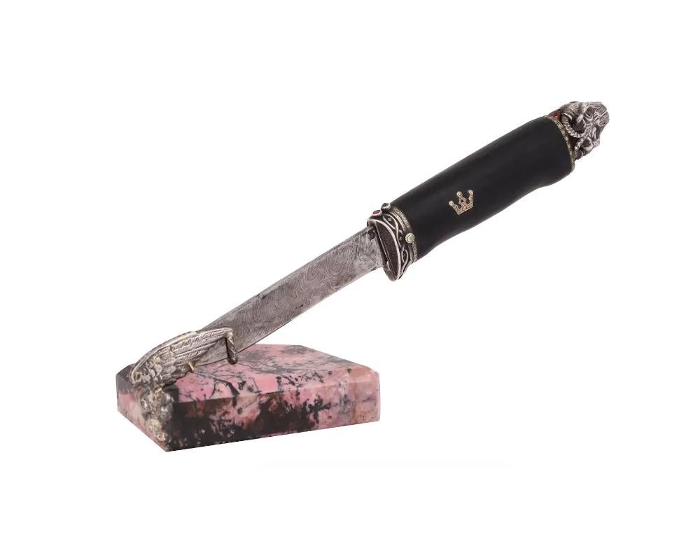 A letter opener knife with a patterned metal blade and a black wood and silver handle with two crowns. The end of the handle is decorated with a silver bull's head. The silver elements on the grip are set with colored diamonds and faceted ruby