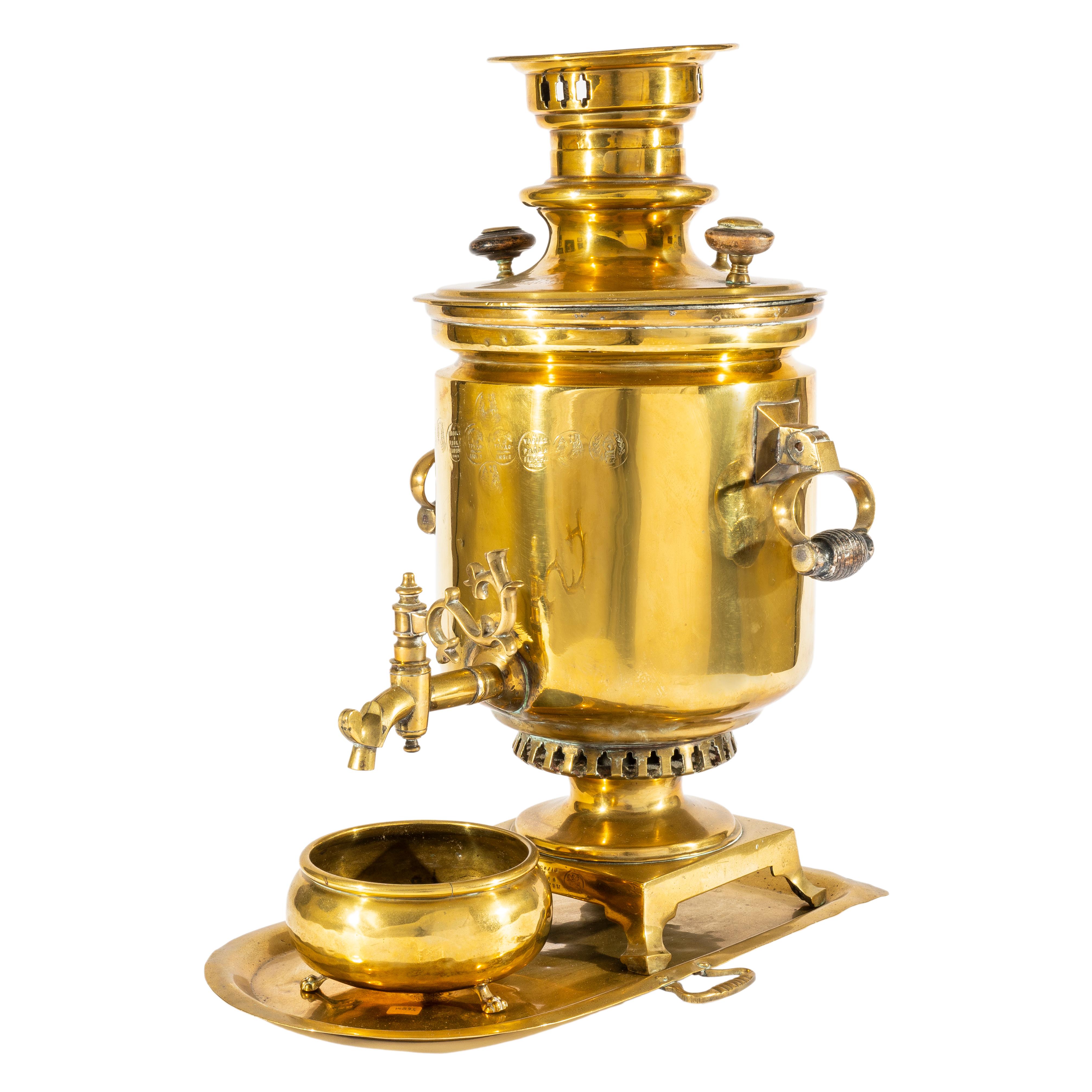 By Tula samovar masters, V.L. Batashev. Of typical form in the Russian imperial style, a classic samovar set tooled in brass comprising a brass samovar, drip bowl and tray. The samovar cylindrical with turned wooden drop handles on a square pedestal