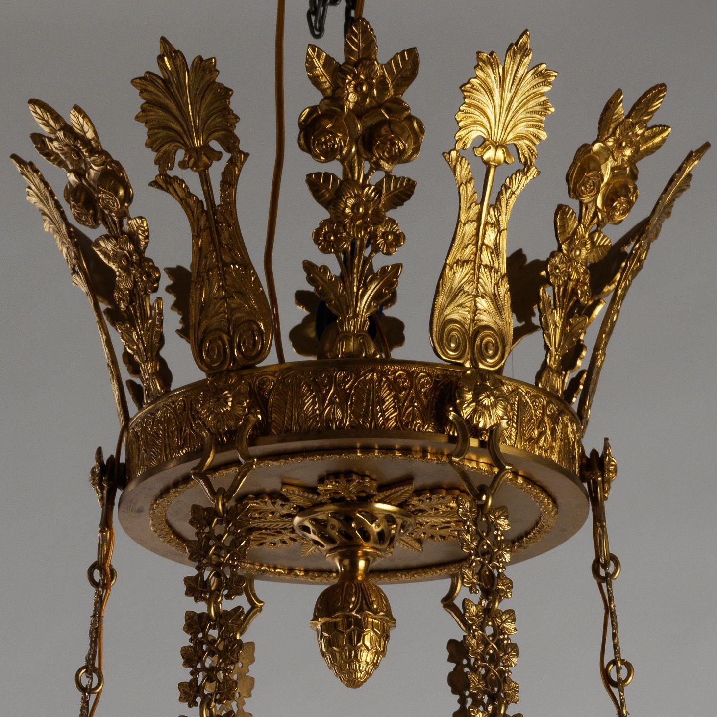 This Russian Empire style gilt bronze chandelier by Gherardo Degli Albizzi features thirty-six lights and a crown decorated with 12 leaves and a pine-cone, from which large chains are leaving downwards. Both rings are decorated with double-armed
