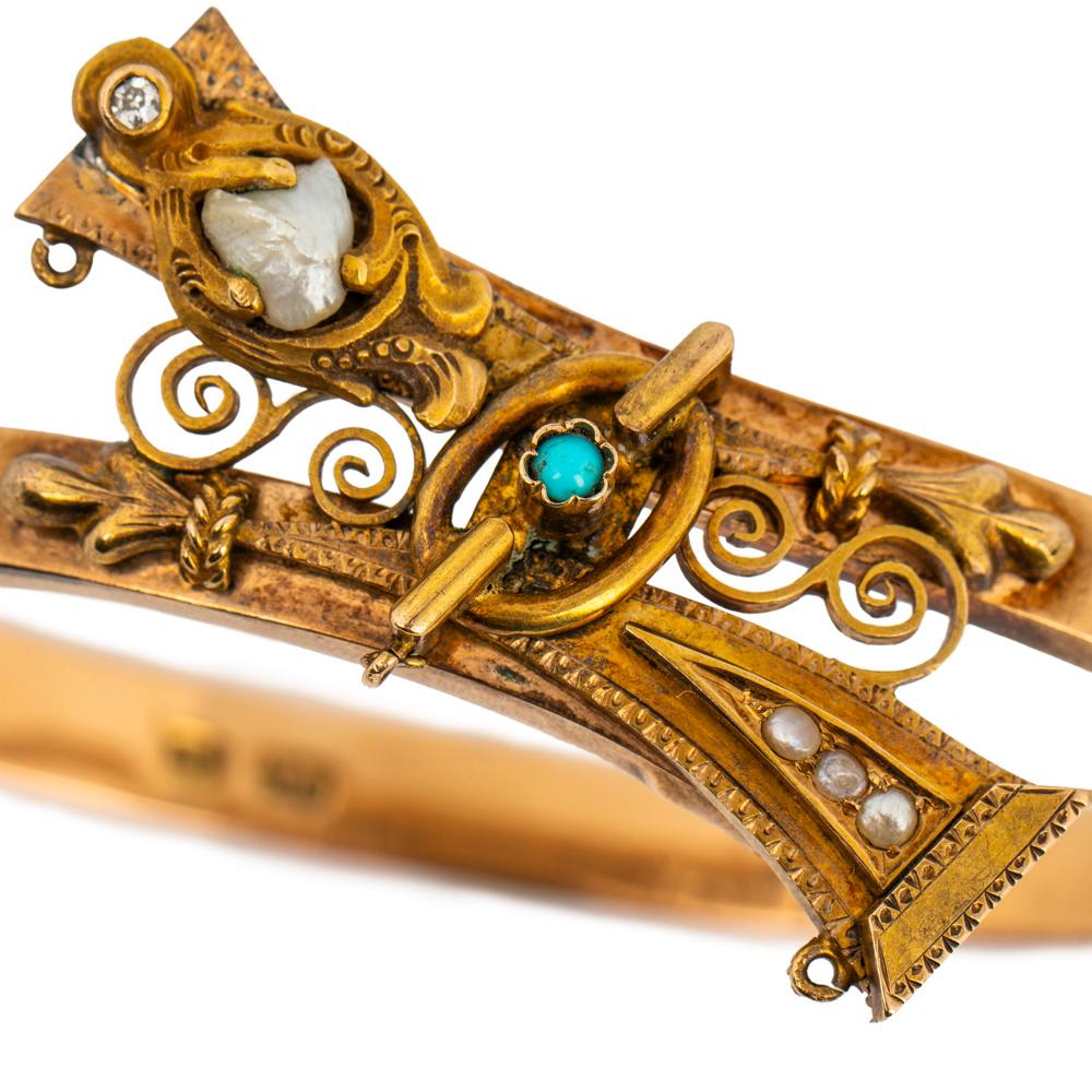 A rare Russian bracelet from the Romanov era, period of Tsar Alexander III, of crossover design applied with Old Russian strapwork motifs and openwork scrolls, this two-color gold bangle from St. Petersburg is set with river pearls, a turquoise and