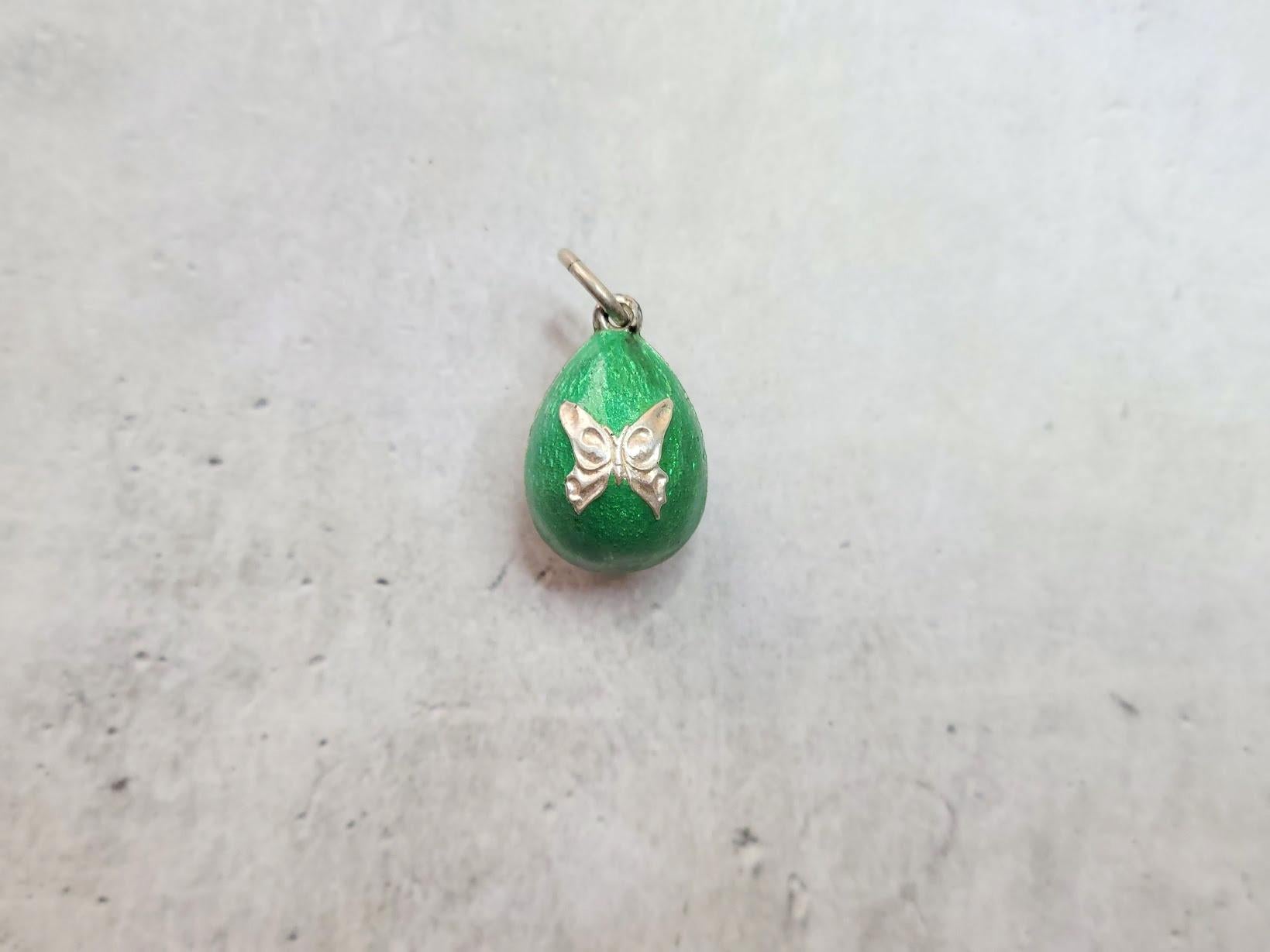 Questo ciondolo Fabergé, un pezzo raro e storicamente significativo, è stato realizzato dal famoso artigiano Phillip Theodore Ringe. Questo uovo d'argento è ricoperto da uno splendido smalto verde arabescato e ornato da due affascinanti farfalle su