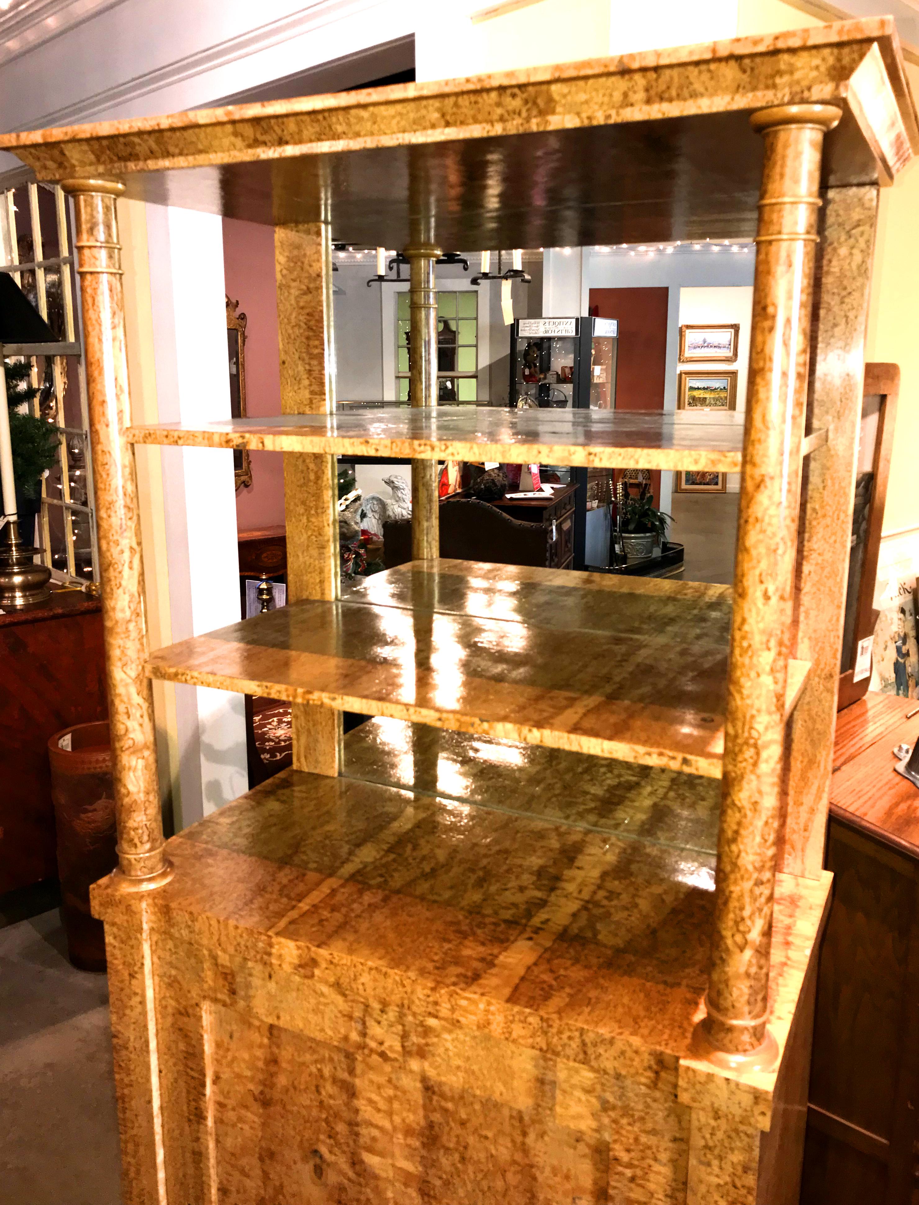 A fine example of a Russian Karelian birch veneered vitrine with molded cornice top over two open upper shelves with mirrored back, supported by two front columns, over a lower case with single paneled door, opening to a single interior shelf, all