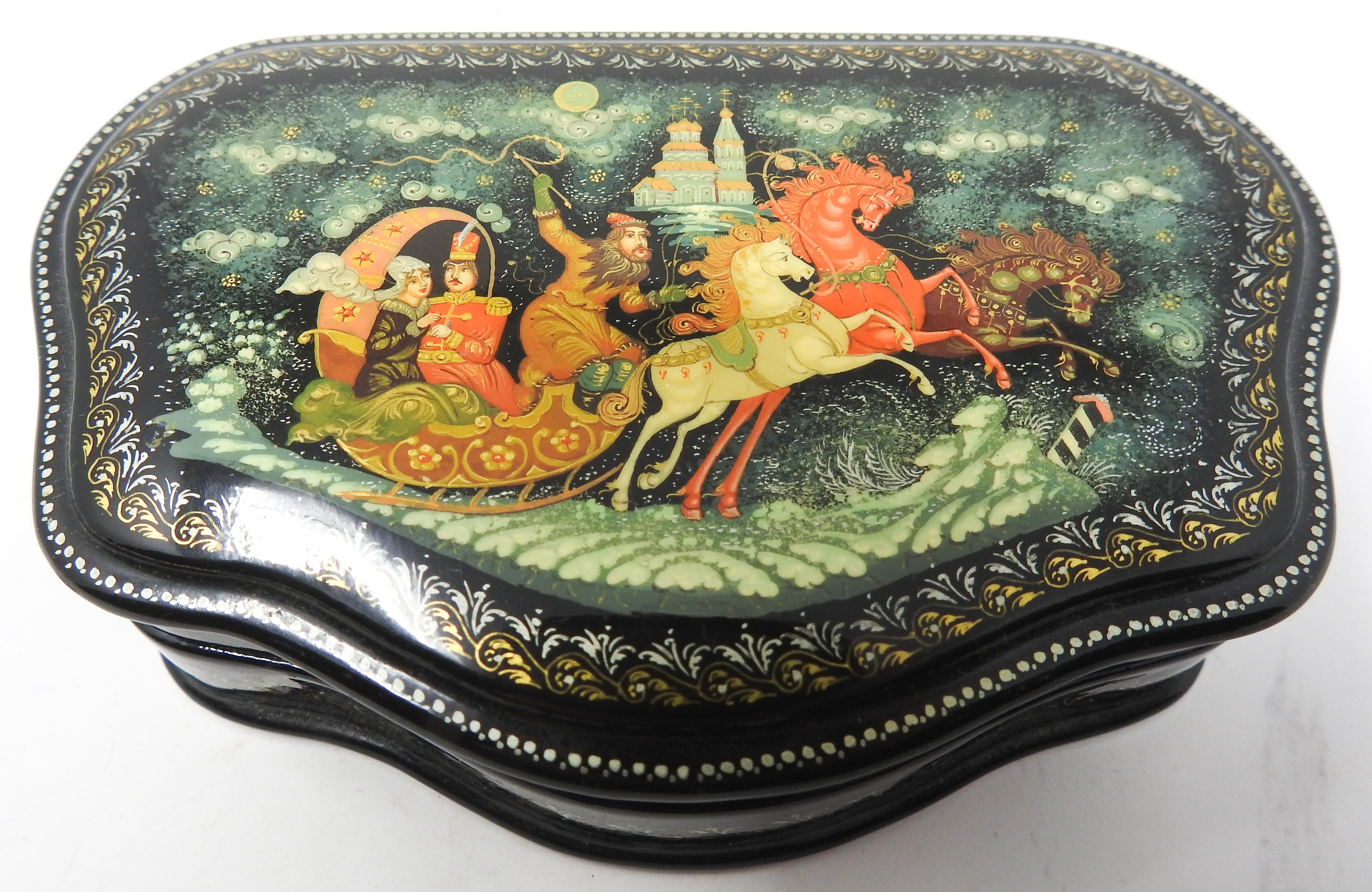 Offering this gorgeous Russian lacquer box. The top depicts a scene of flying horses pulling a chariot holding three people. Off in the background is a castle and the sky has clouds of swirls. Surrounding that is gold and silver filigree. The same