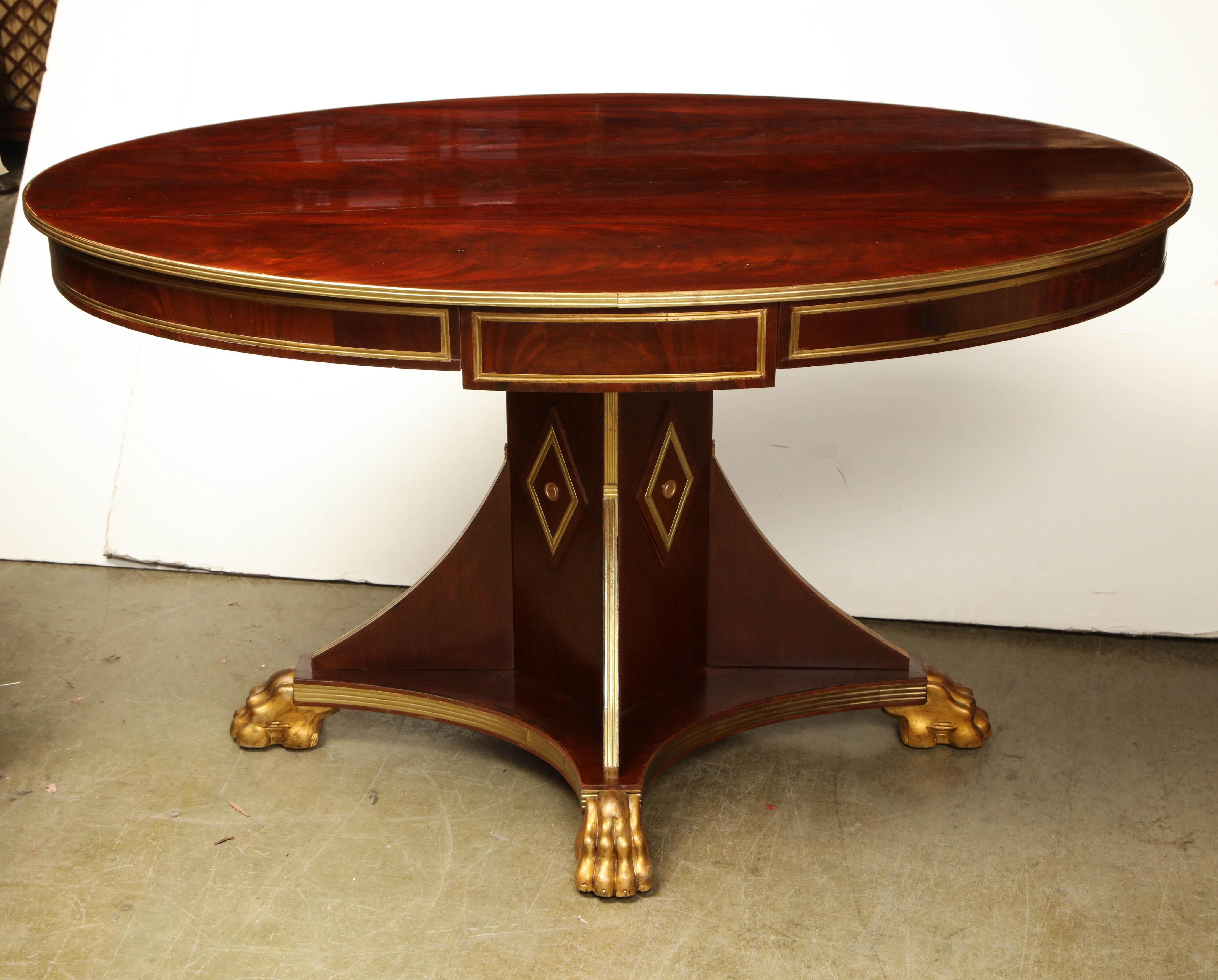 An unusual Russian neoclassic mahogany oval center table with brass trim and on a parcel-gilt paw foot pedestal base.