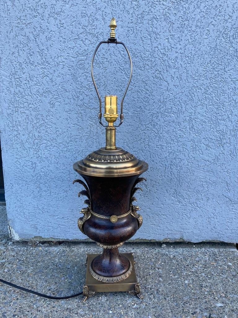 Neoclassical style table lamp in the form of a leather clad urn with bronze peacocks on either side joined by a decorative rope border with circular bosses in the center. The base with acanthus leaf decoration and paw feet. 
I've seen many lamps in