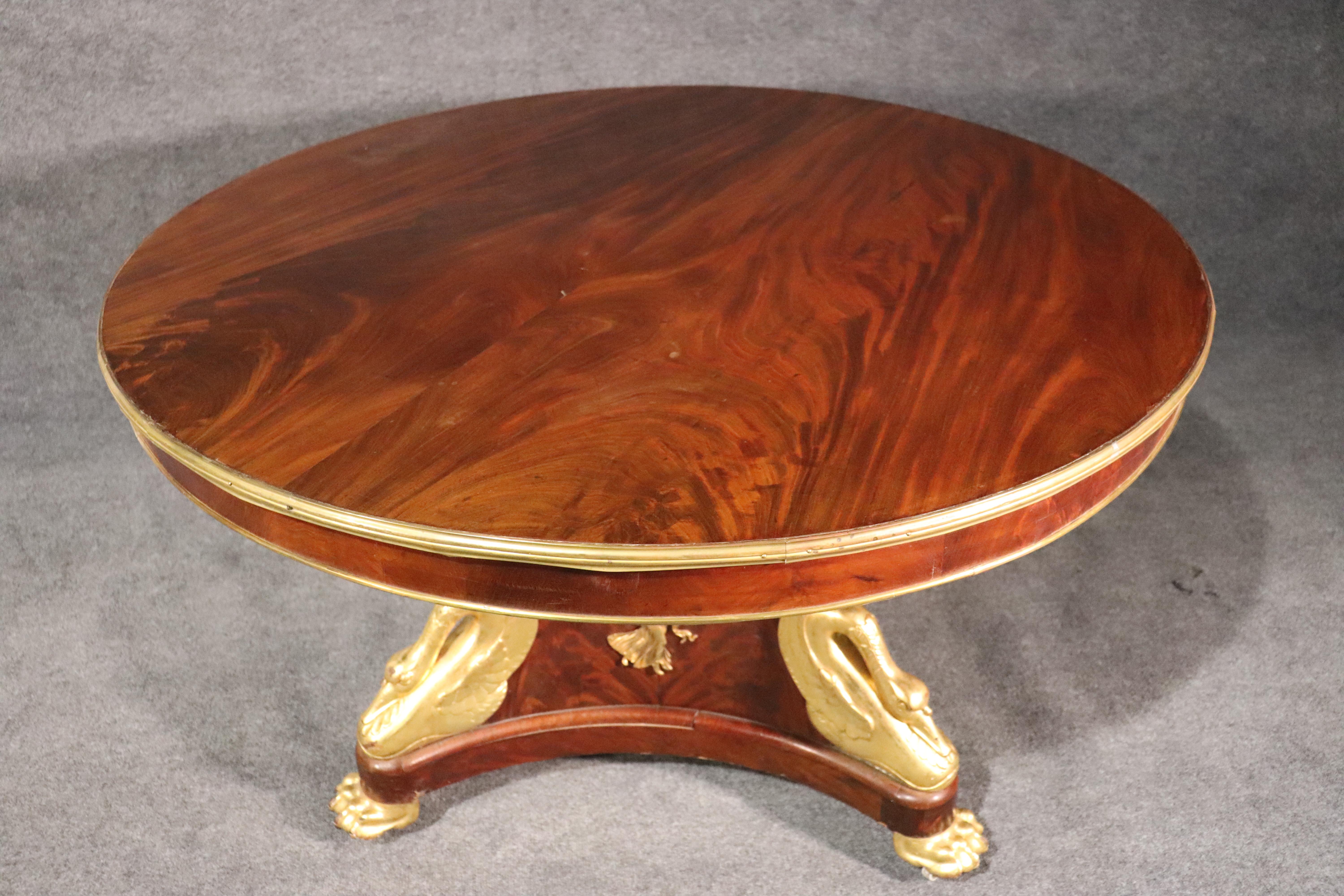 This is a rare solid mahogany carved center table with a large round top with polished bronze trim at the top and a bronze angel at the base. The table features water-gilded swans, which is the brightest and most metallic form of gold leafing. The
