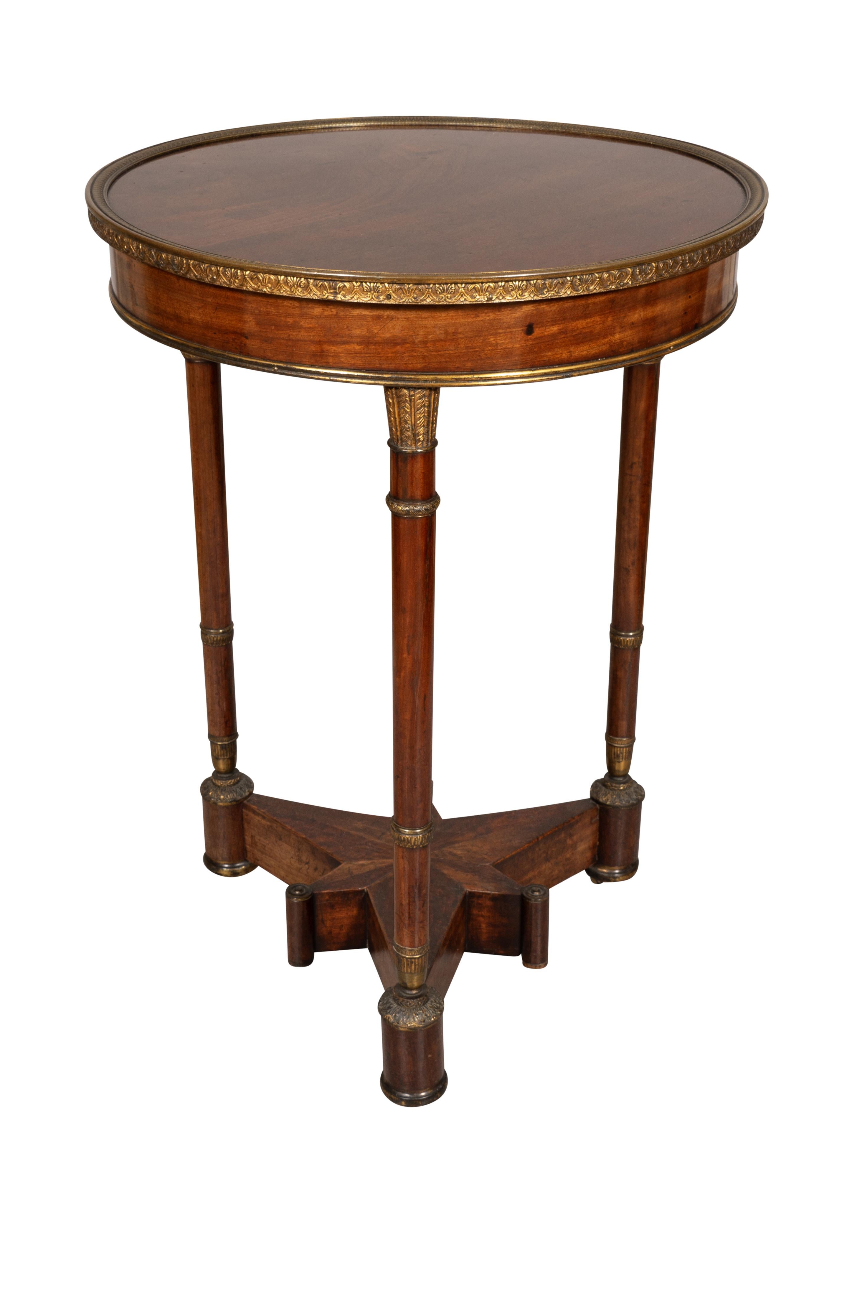 With circular top with cast gilt bronze border with three columnar supports headed by gilt bronze clustered arrow quills. Lower star form shelf with compass inlay. Casters.