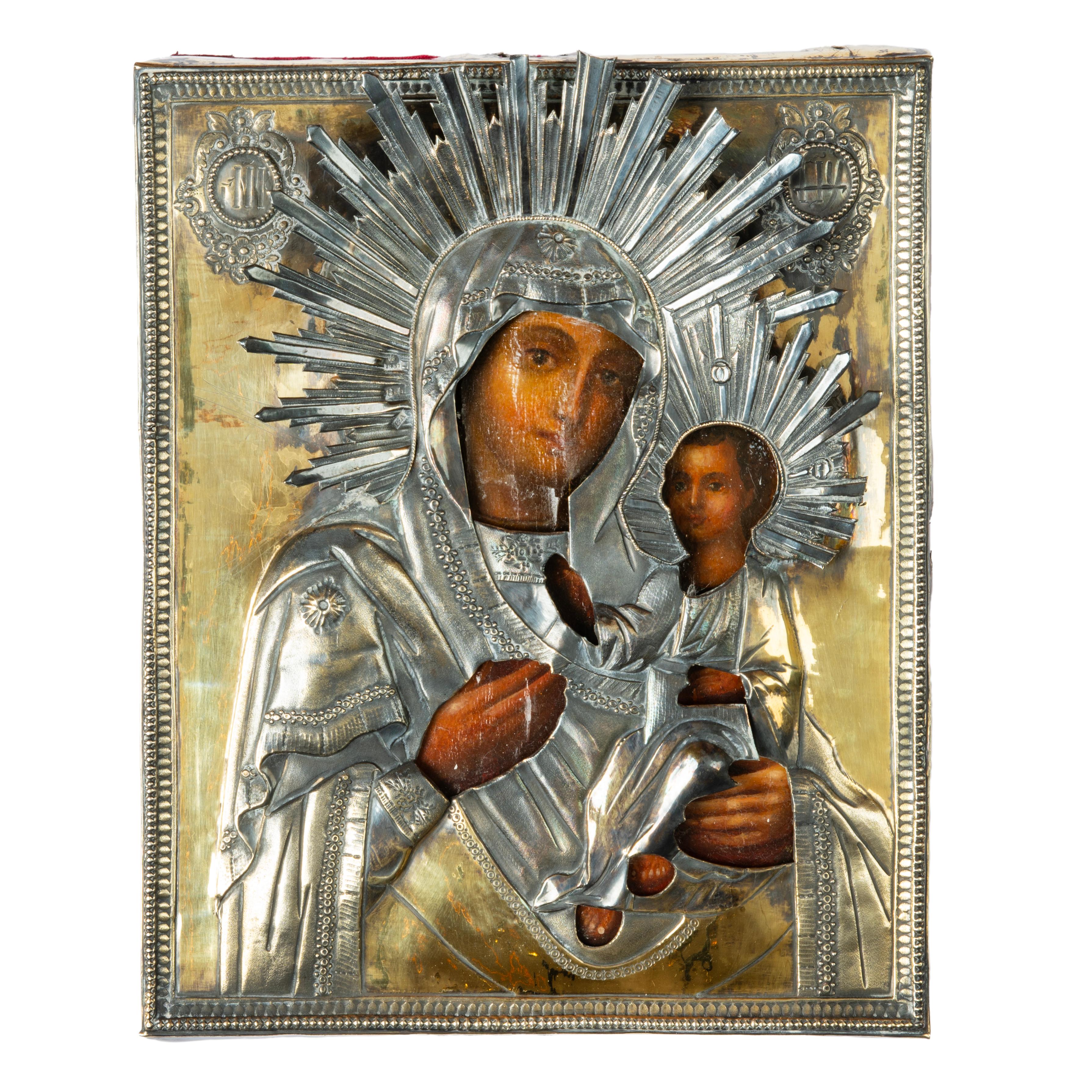A beautiful Pushkin-era silver icon depicting the Tikvin Mother of God, covered with a silver-gilt oklad, with repoussé garments, veil and applied haloes of sunburst design. The Christ child seated to the Virgin’s left, his hand raised in blessing,