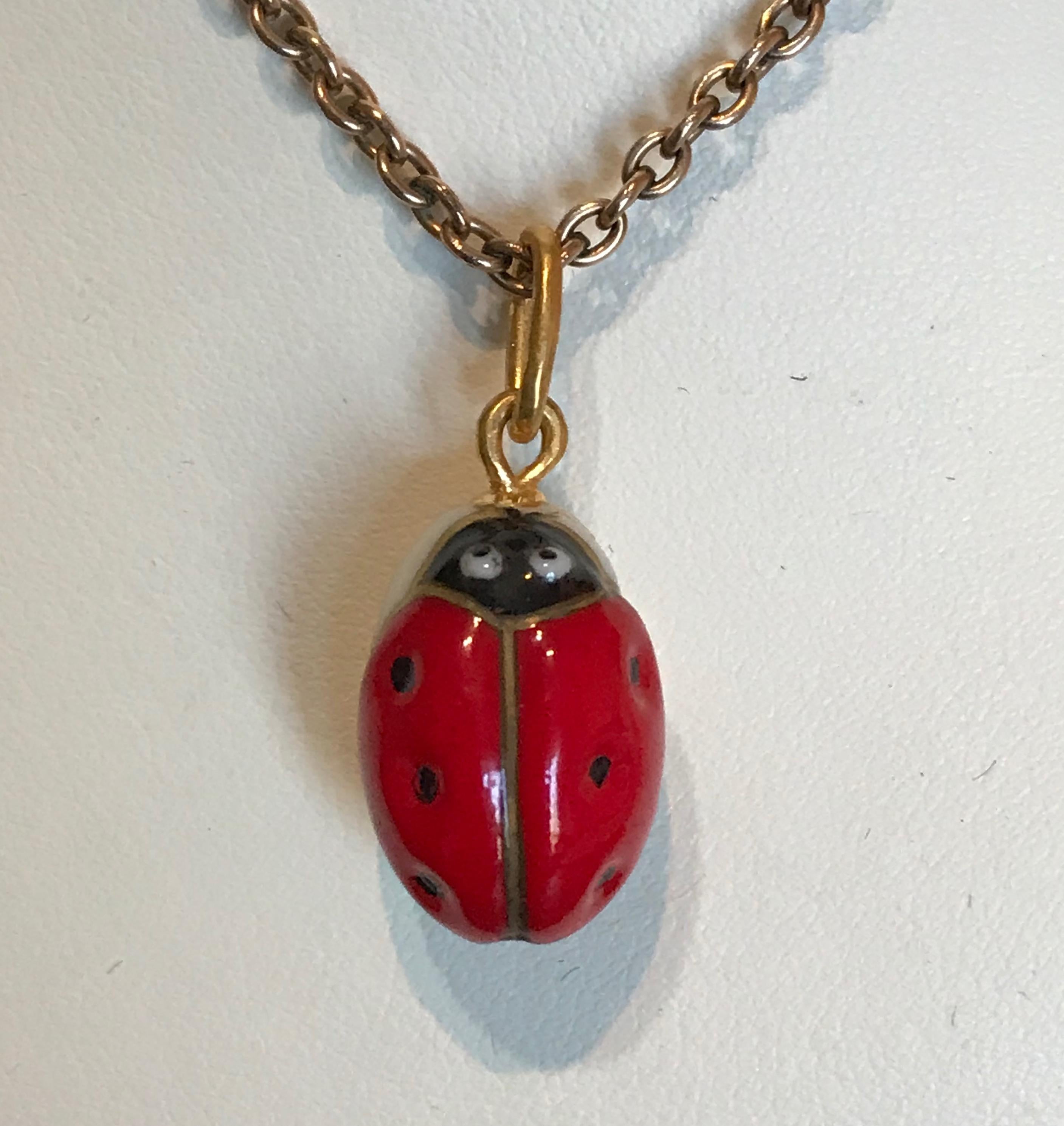 A beautiful porcelain miniature egg pendant, the front featuring a slightly domed bright red lady bug, the reverse detailing its black legs on a white opalescent ground. Fitted with a large oval gilded suspension ring to accommodate different size